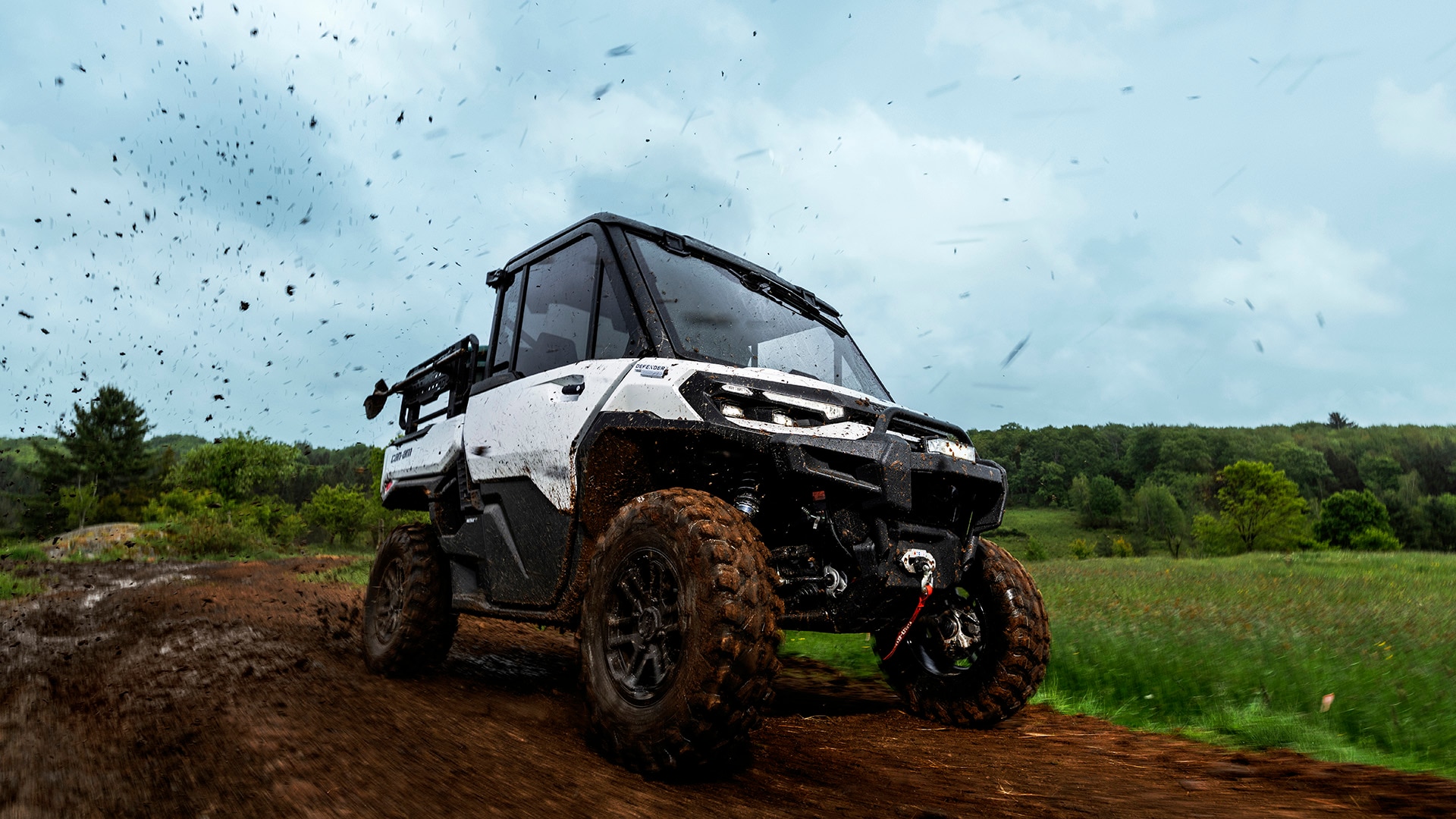 A 2026 Can-Am Defender HD11 white hybrid side-by-side vehicle driving on a muddy road