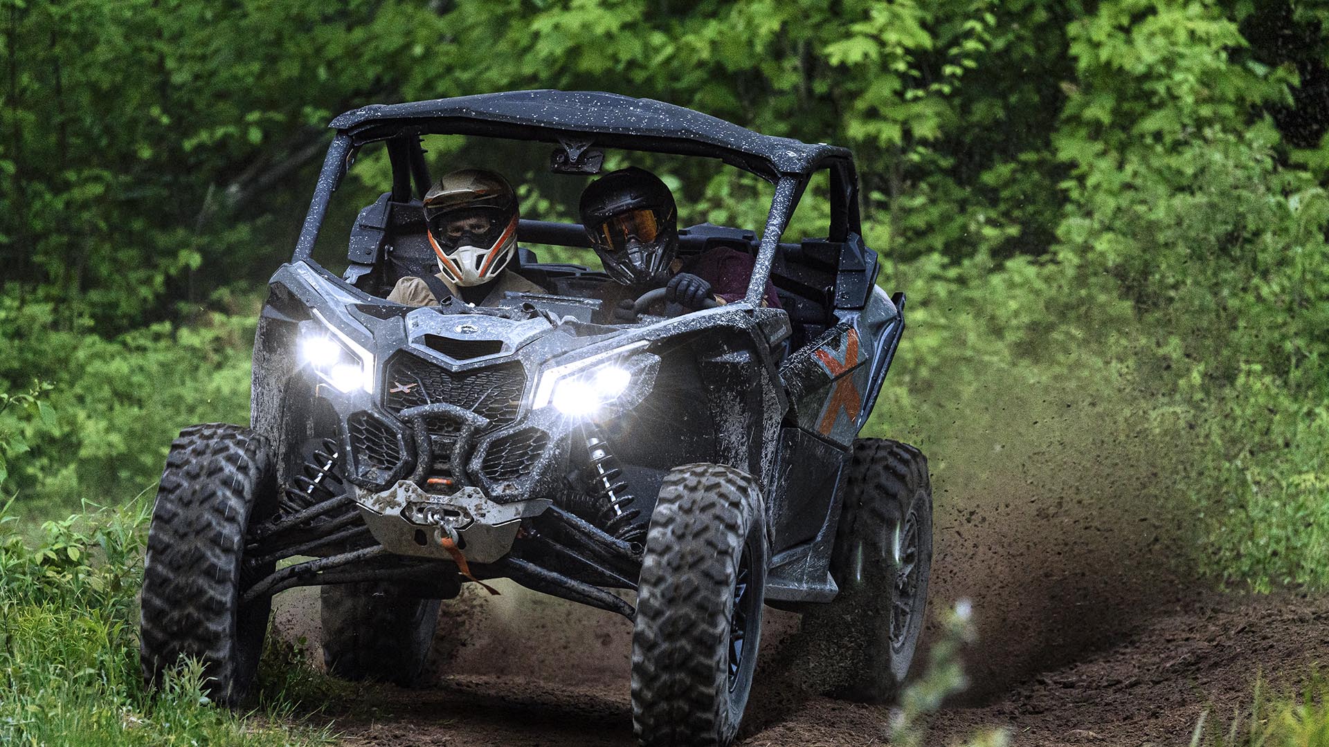 Two riders in a Can-Am Maverick X3 X Turbo side-by-side on a dirt trail 