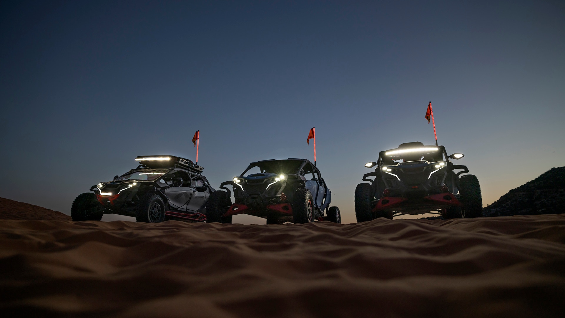 Three Can-Am Maverick with bright headlights and tailights in the sand during the night