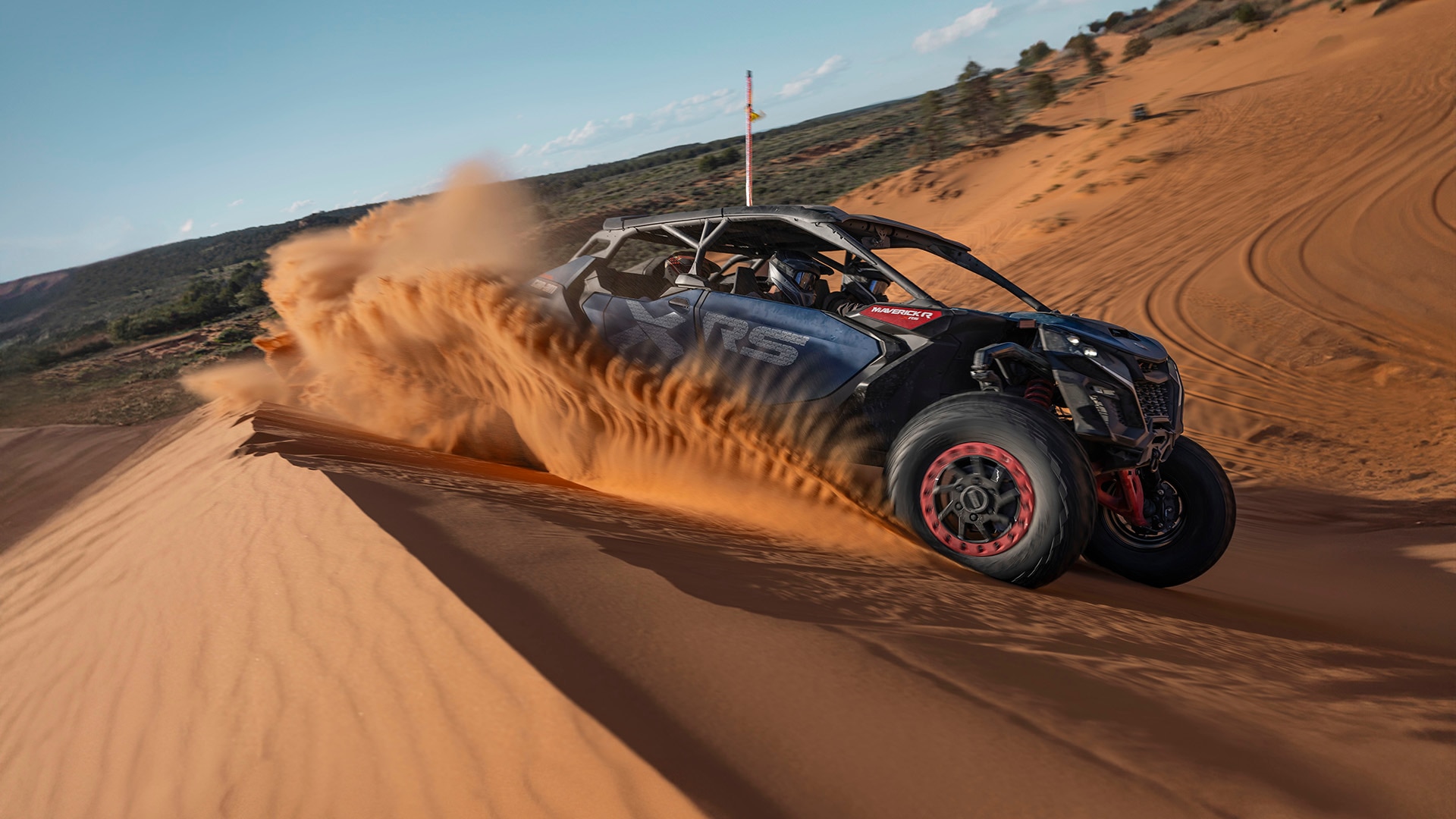 Can-Am Maverick R MAX RS rolling down a sand dune on a sunny day