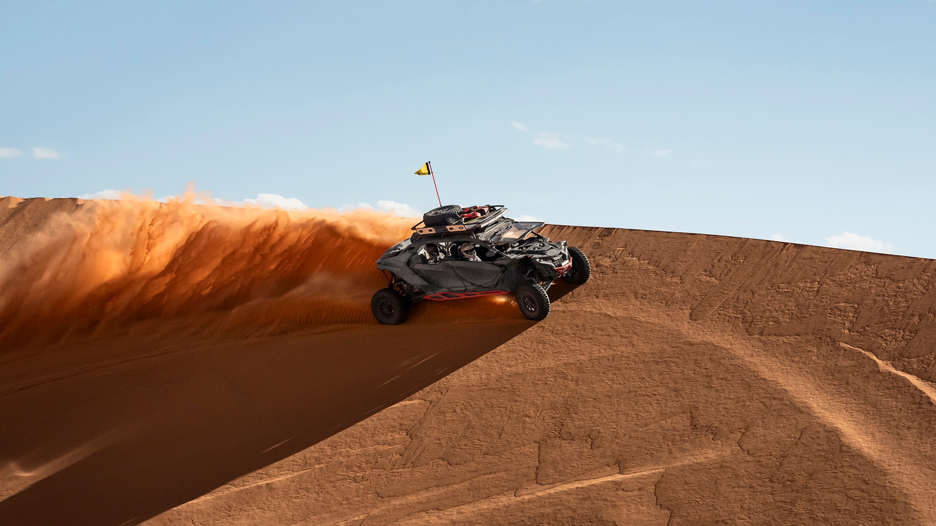 A Can-Am Maverick R MAX X RS riding in the sand leaving sand behind it