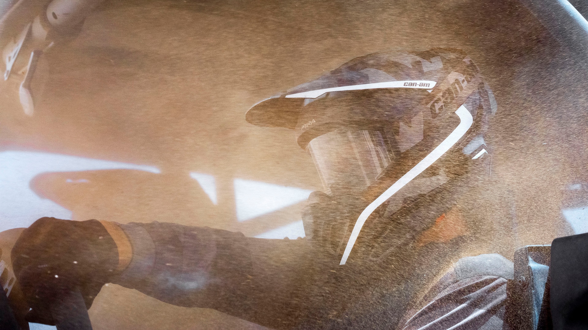 Two drivers wearing Can-Am helmets inside a Can-Am Maverick R side-by-side vehicle