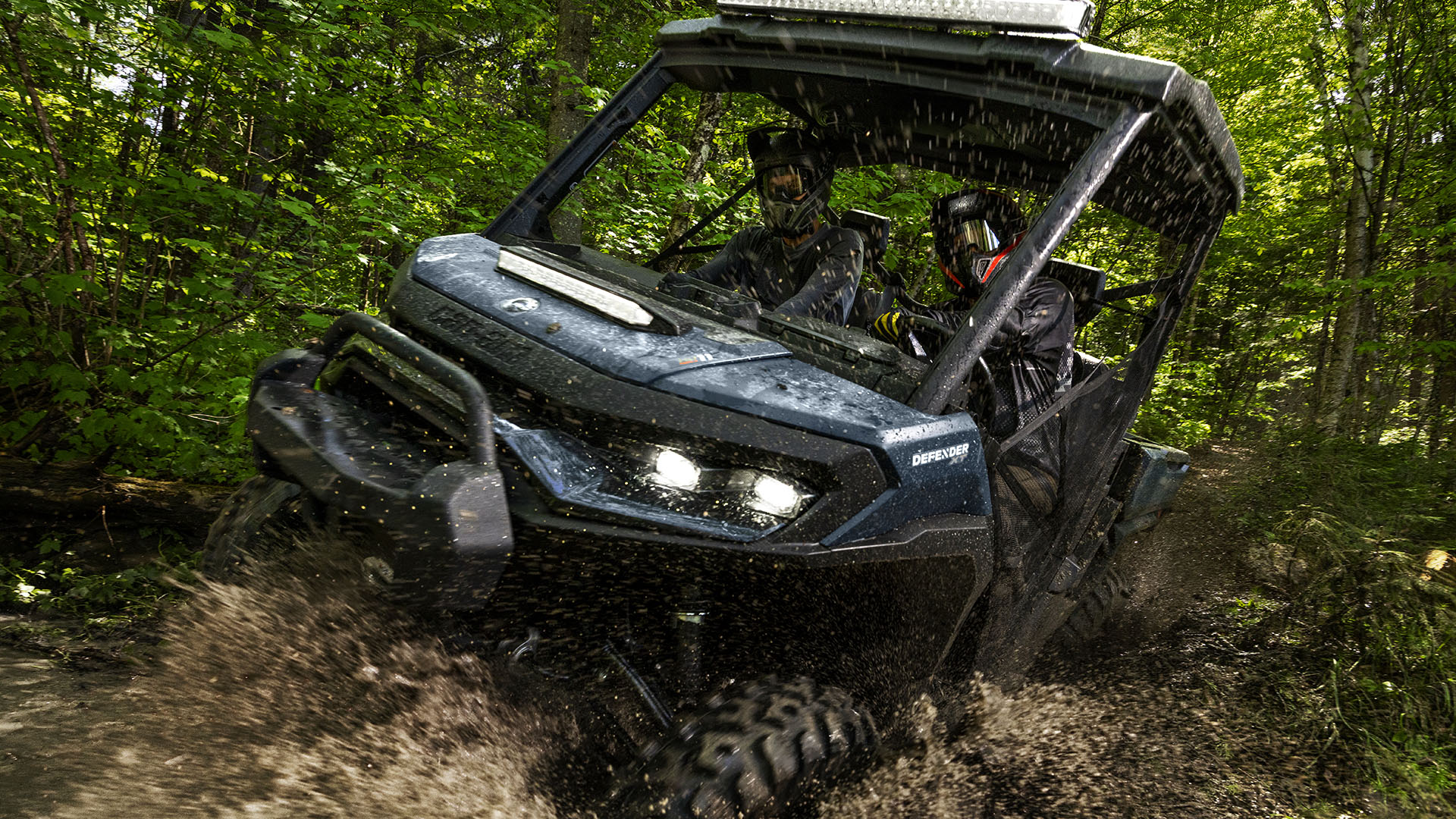 Two riders in the 2026 Can-Am Defender HD11 on a muddy trail