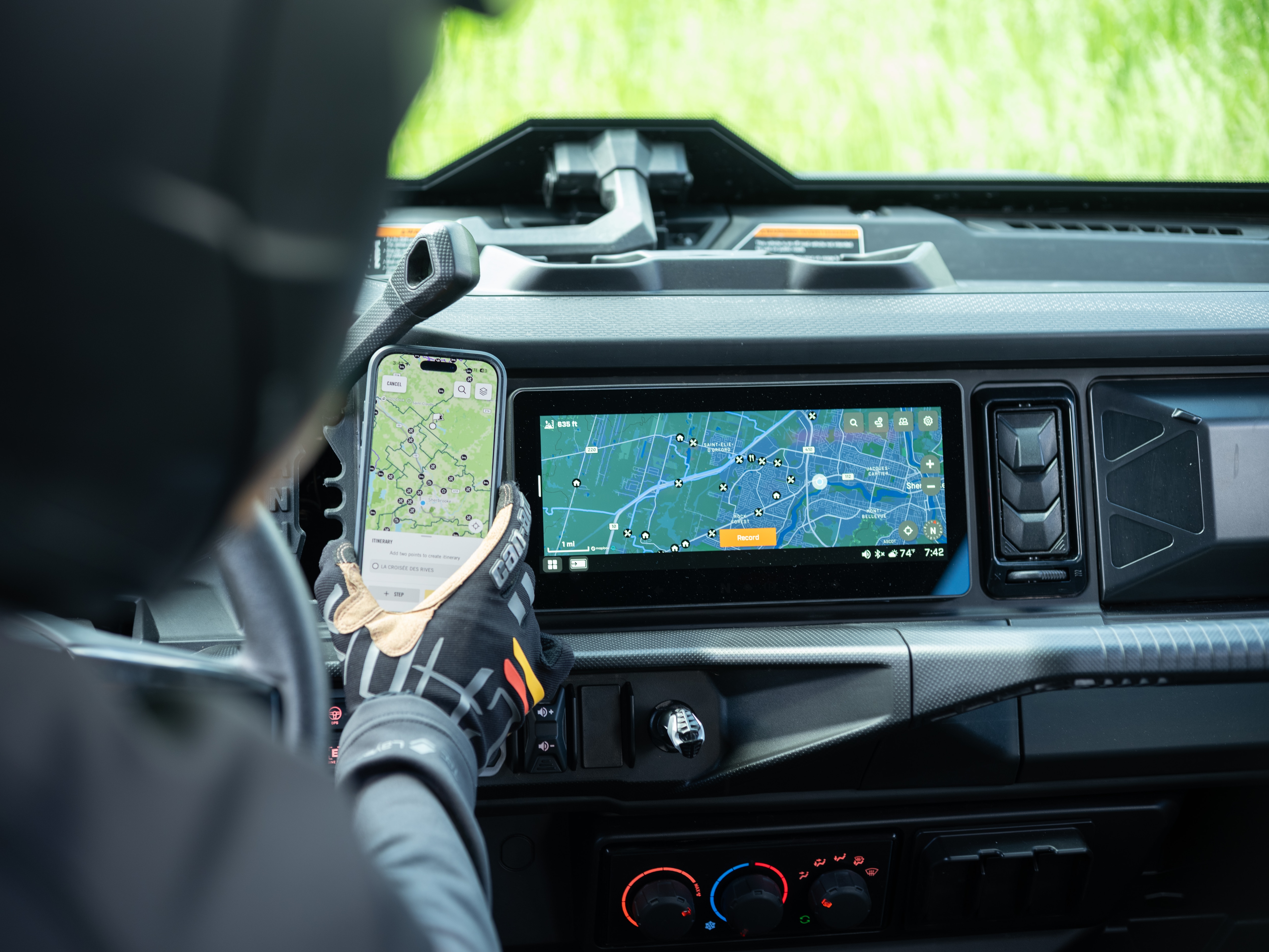 A rider sitting inside a Can-Am SxS comparing the map on a phone to the 10.25-inch touchscreen display
