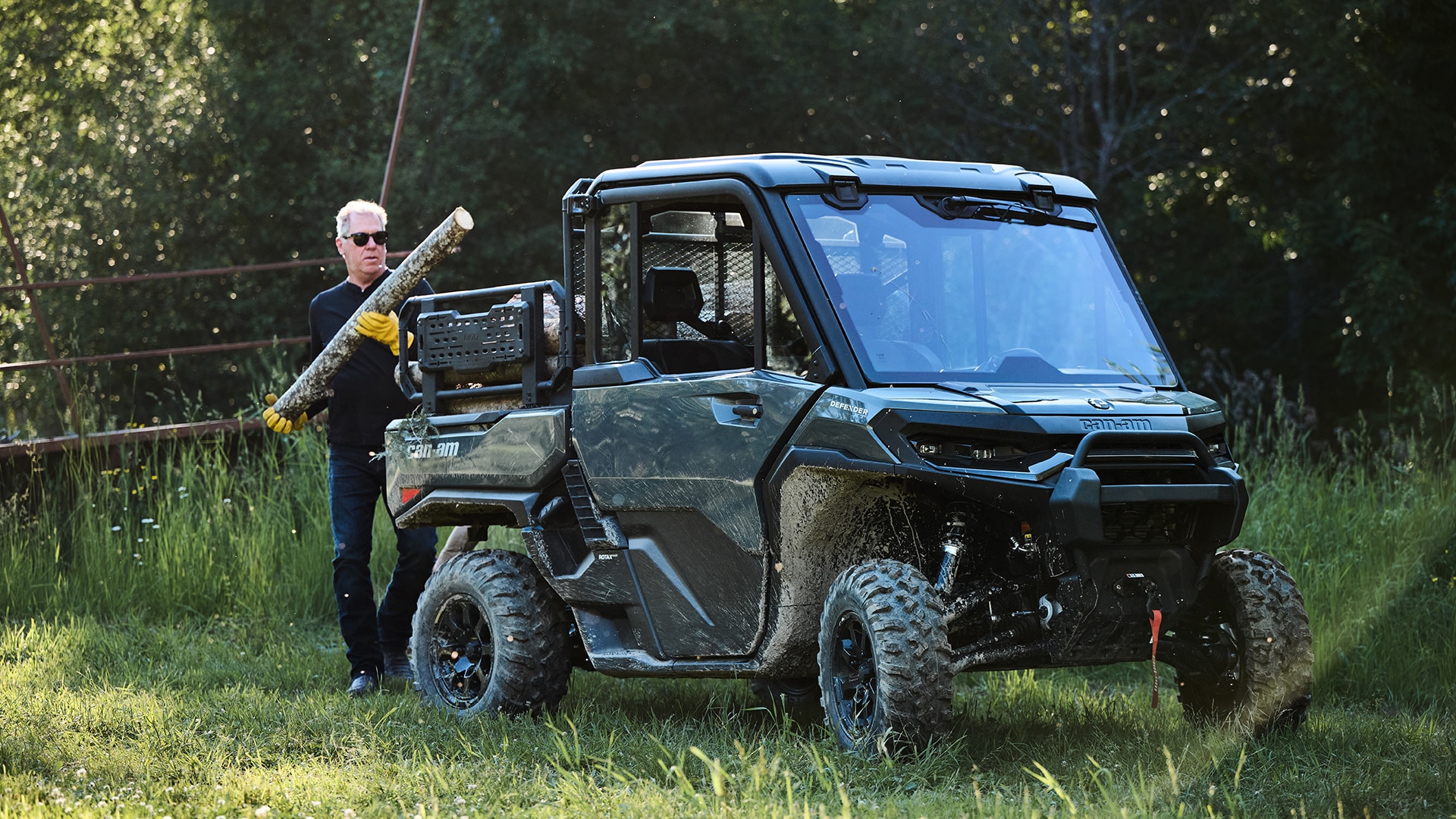 Un hombre colocando troncos en la caja de su vehículo side-by-side Can-Am Defender