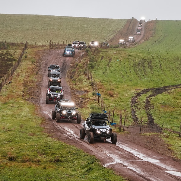 Um comboio com veículos Can-Am avançando em fila indiana por uma estrada de terra.