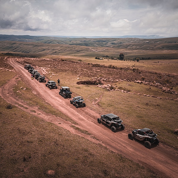  Uma vista aérea de um grande comboio com veículos Can-Am avançando em fila indiana por uma estrada.