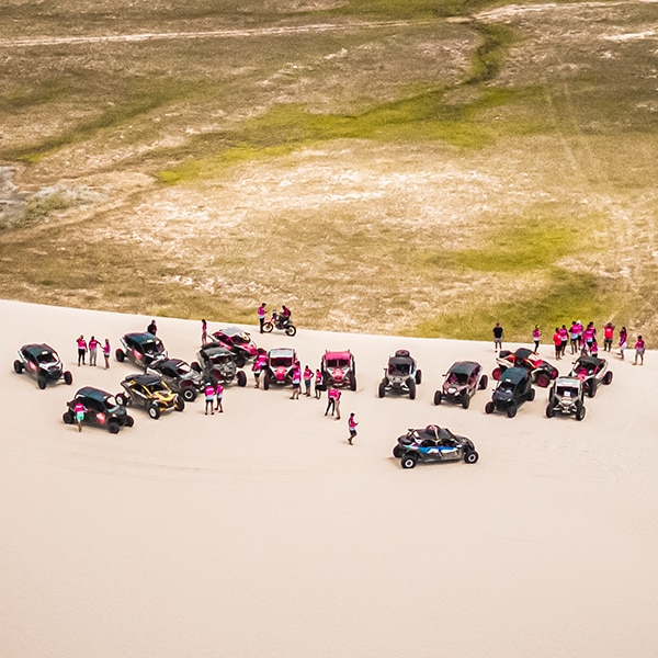 Comboio com veículos Can-Am estacionados em grupo na areia.
