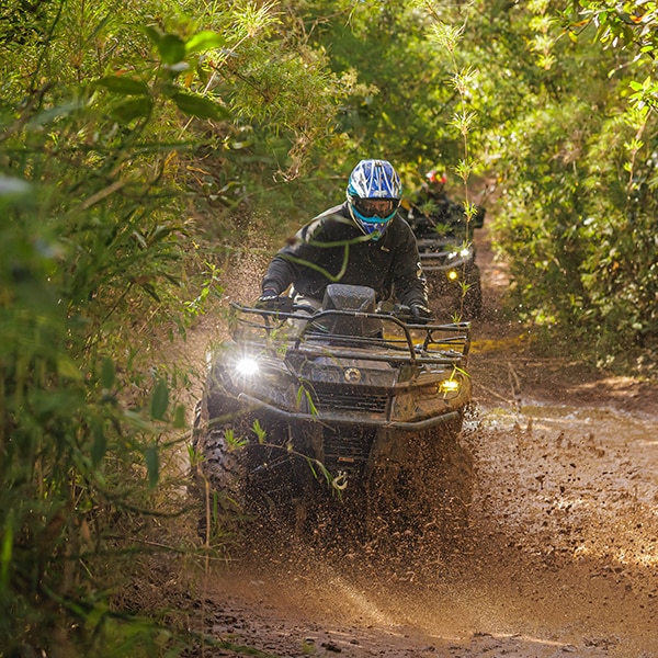Dois quadriciclos Can-Am avançando por uma trilha estreita de terra e lama.