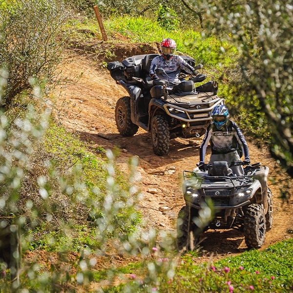 Dois quadriciclos Can-Am descendo em fila por uma trilha sinuosa e inclinada de terra. 