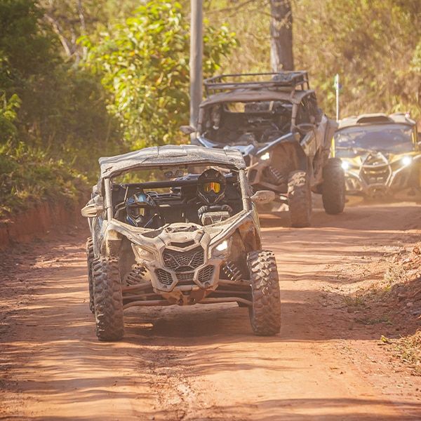 Um comboio de veículos Can-Am avançando de frente por uma estrada de terra.