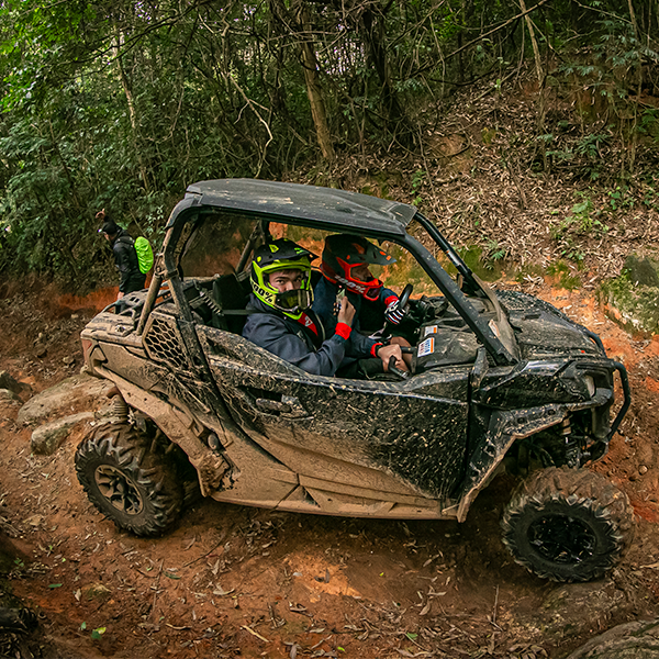 Veículo Can-Am com marcas de lama posicionado em trilha de terra.