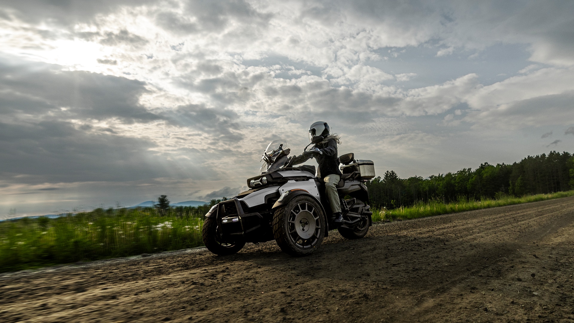A motorcyclist riding his Can-Am Canyon three-wheeled motorcycle on a dirt road, next to a field