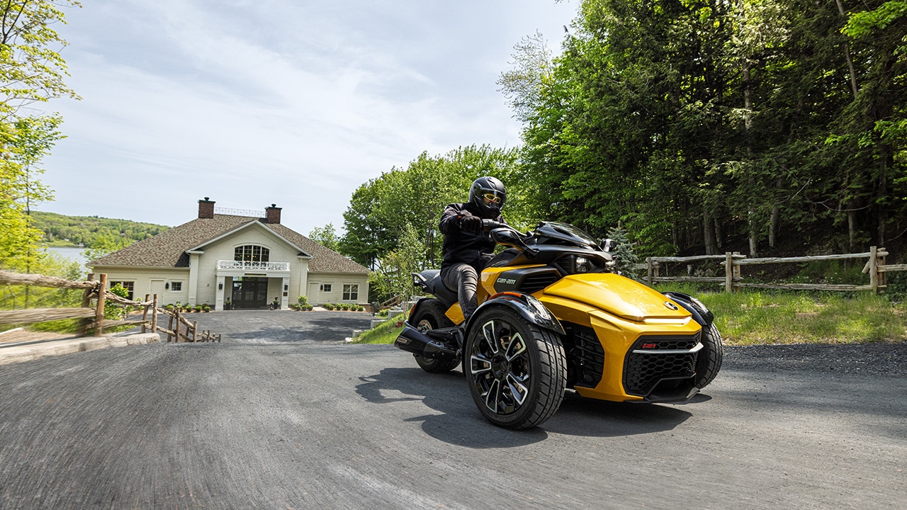 A yellow 2026 Can-Am Spyder F3-S leaving a beautiful house on the waterfront