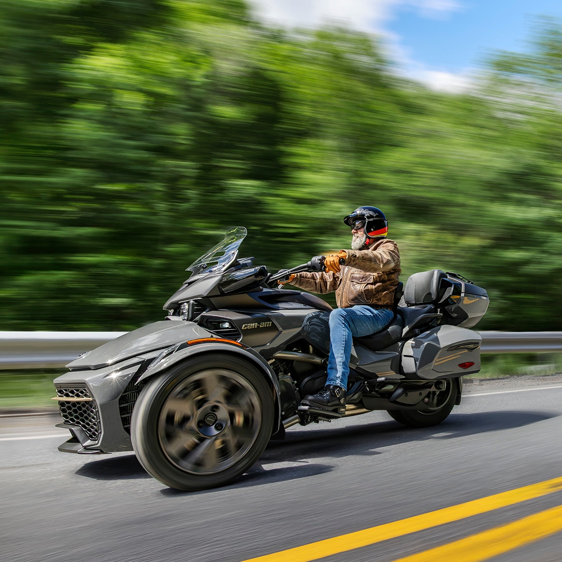 Un homme sur son trois roues Can-Am Spyder 2027 roulant sur une route pavée avec des arbres en arrière-plan