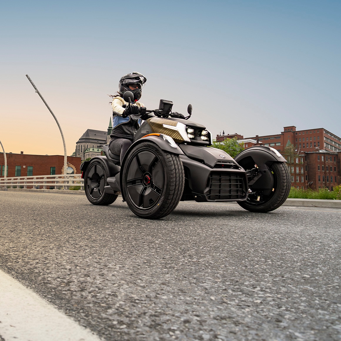 Un Can-Am Ryker 2027 roulant sur un pont avec une ville en arrière-plan