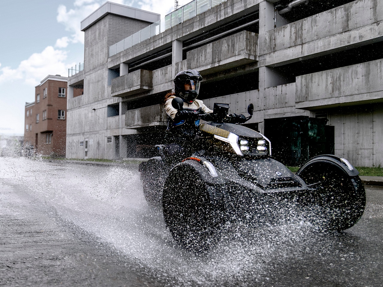 Un véhicule Can-Am Ryker 2027 roulant dans l’eau devant un stationnement à étages