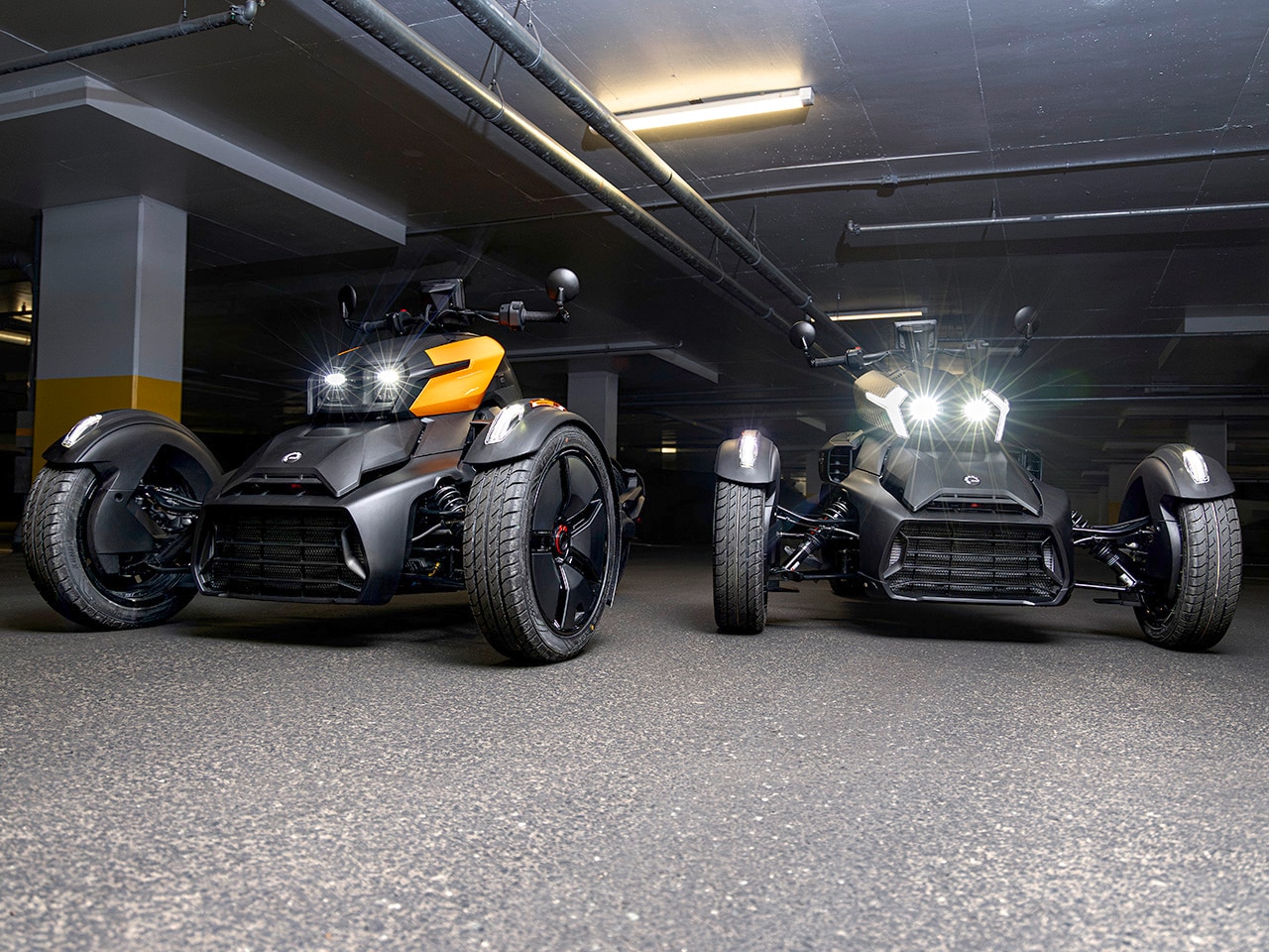 Deux véhicules 3 roues Can-Am Ryker 2027 avec les phares allumés dans un stationnement à étages