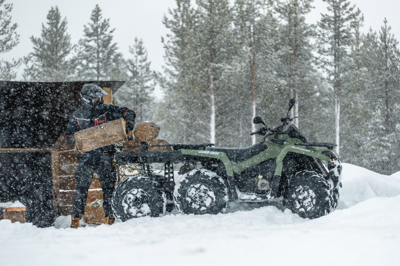 Un trabajador cargando madera en su Can-Am Outlander 6x6 en un entorno nevado.