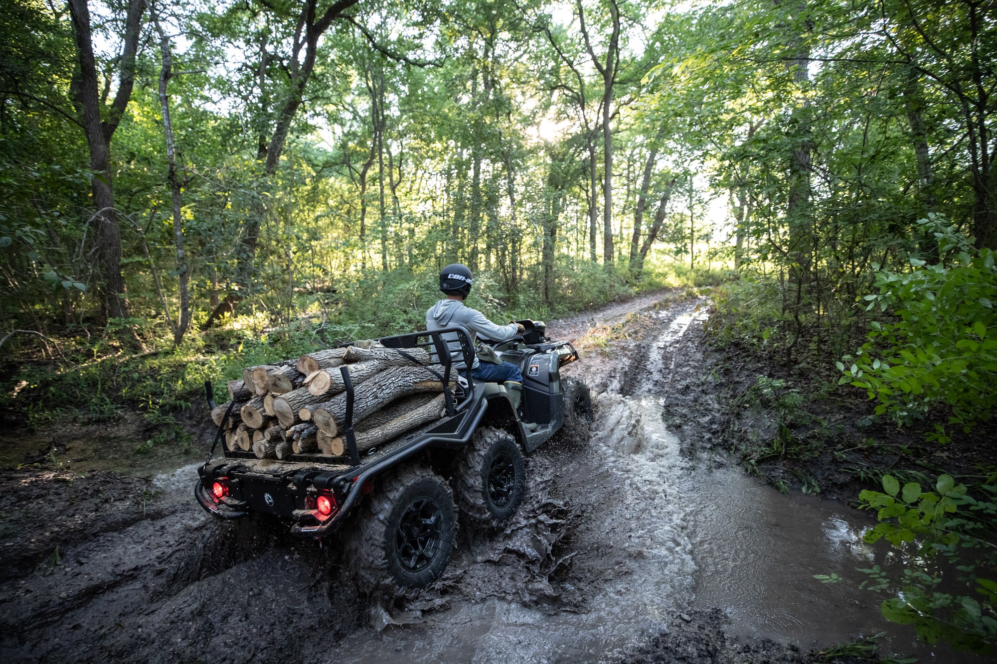 Man riding a Can-Am Outlander 6x6 ATV in the mud with wood in the rear rack