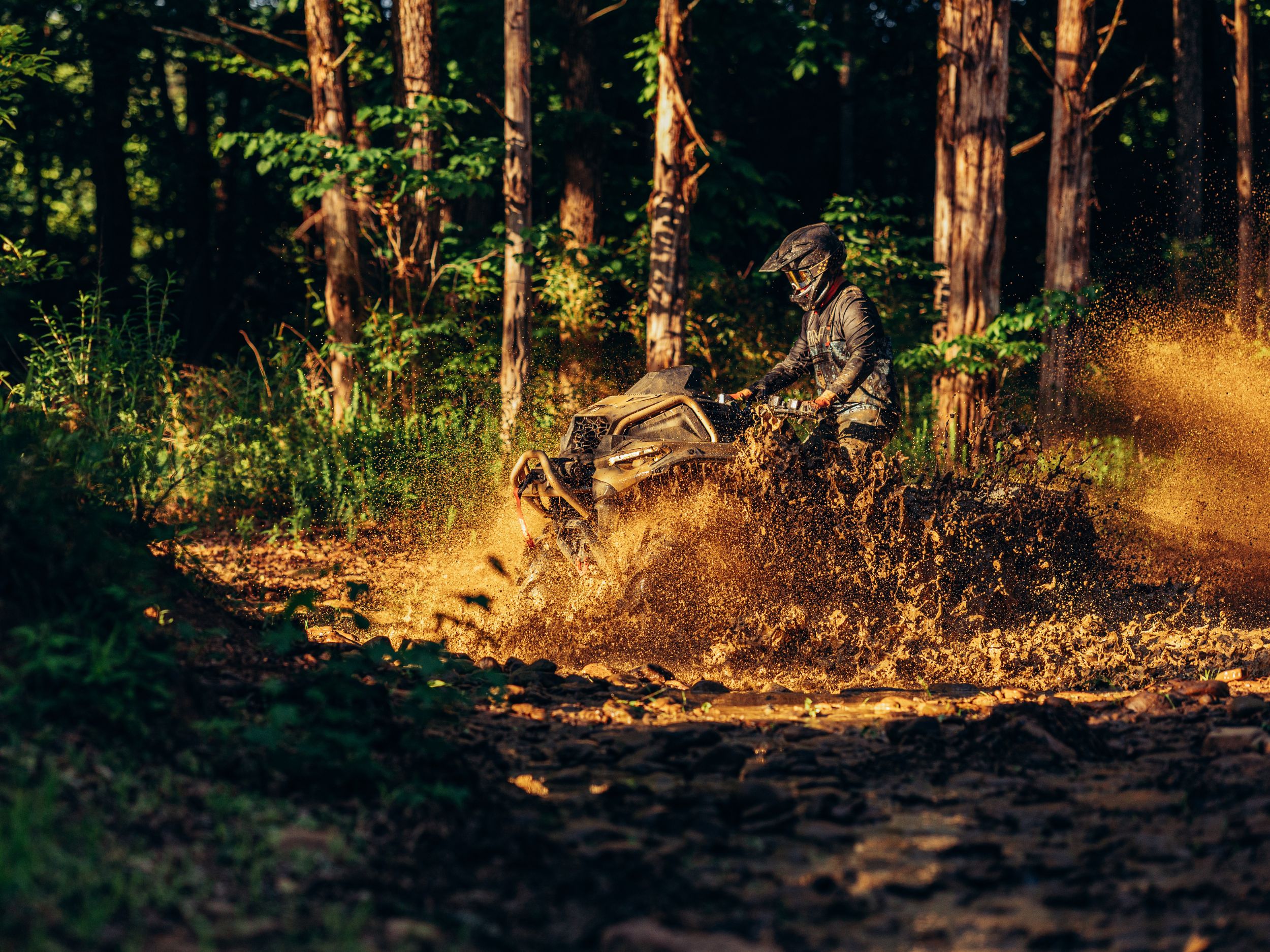 Man rijdt op een Can-Am Outlander Quad, rechtopstaand, in diepe modder