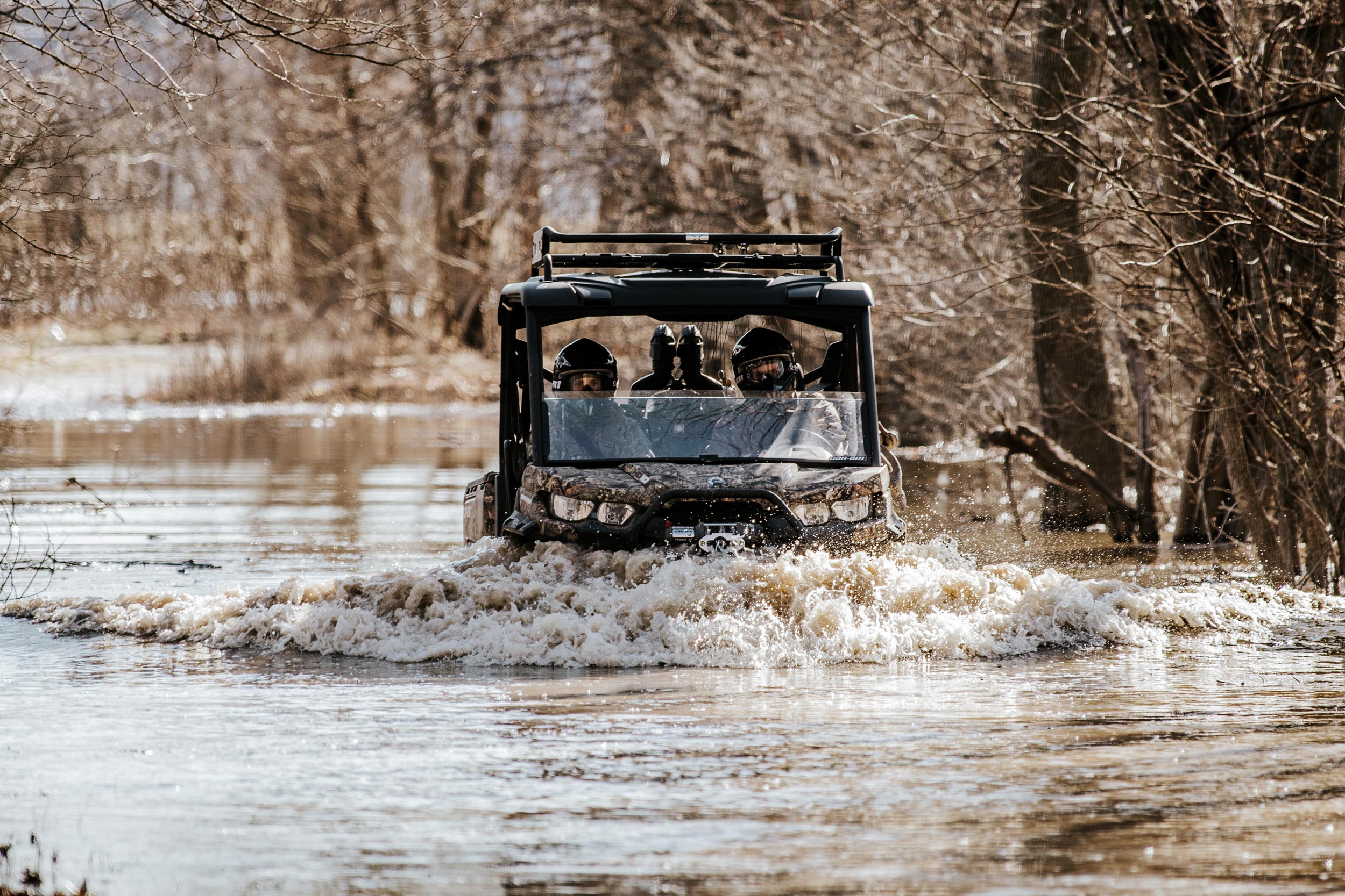 Deux hommes qui conduisent un Can-Am Defender Mossy Oak Edition dans l'eau
