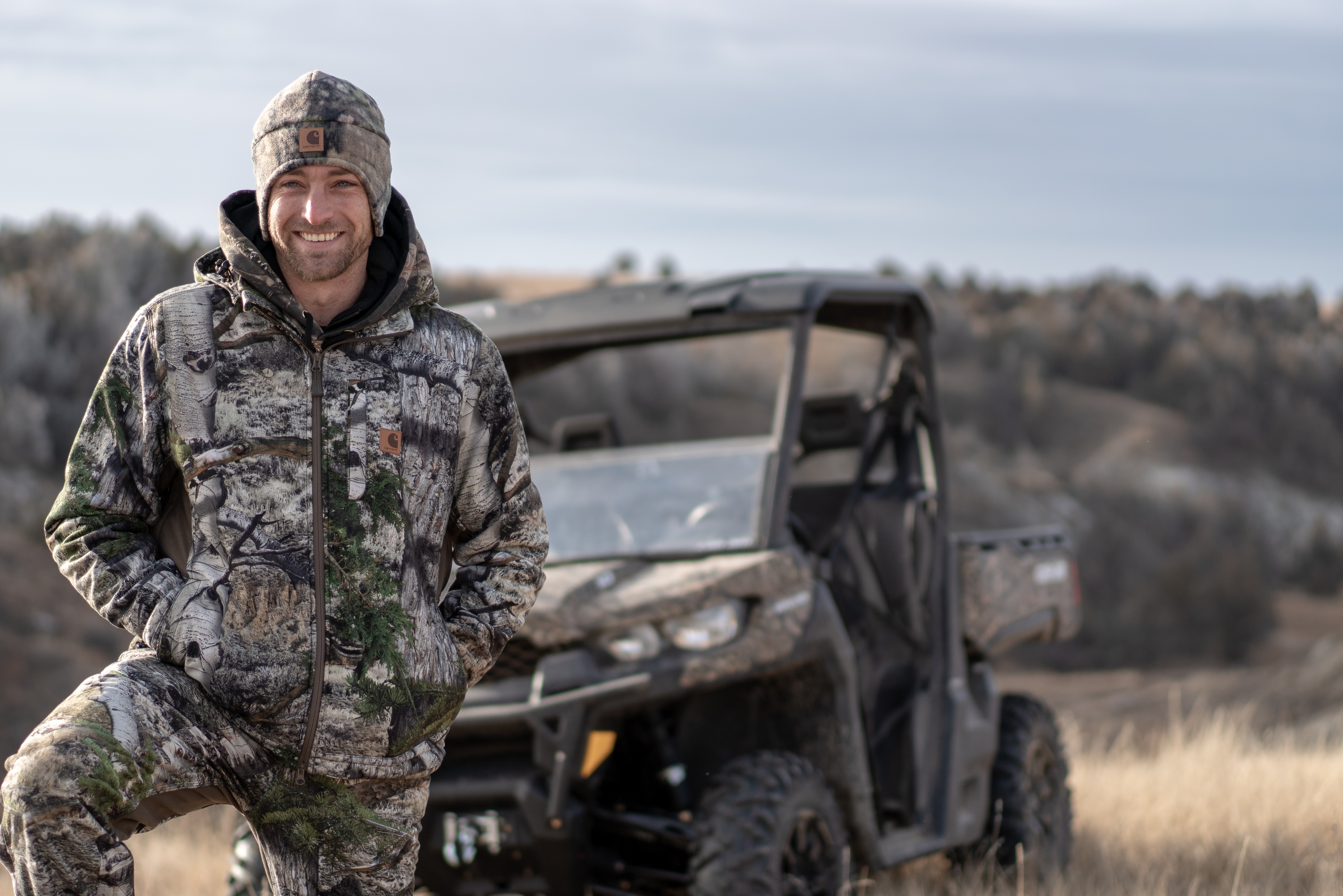 A portrait photo of a hunter with a Can-Am Defender in the back