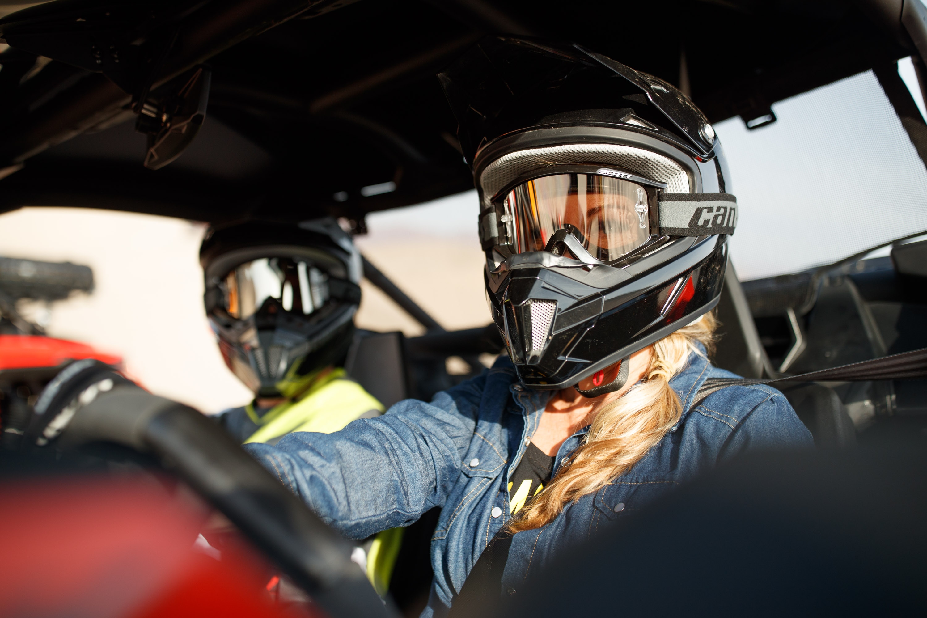 A woman riding a Can-Am side-by-side with Can-Am helmet and goggles