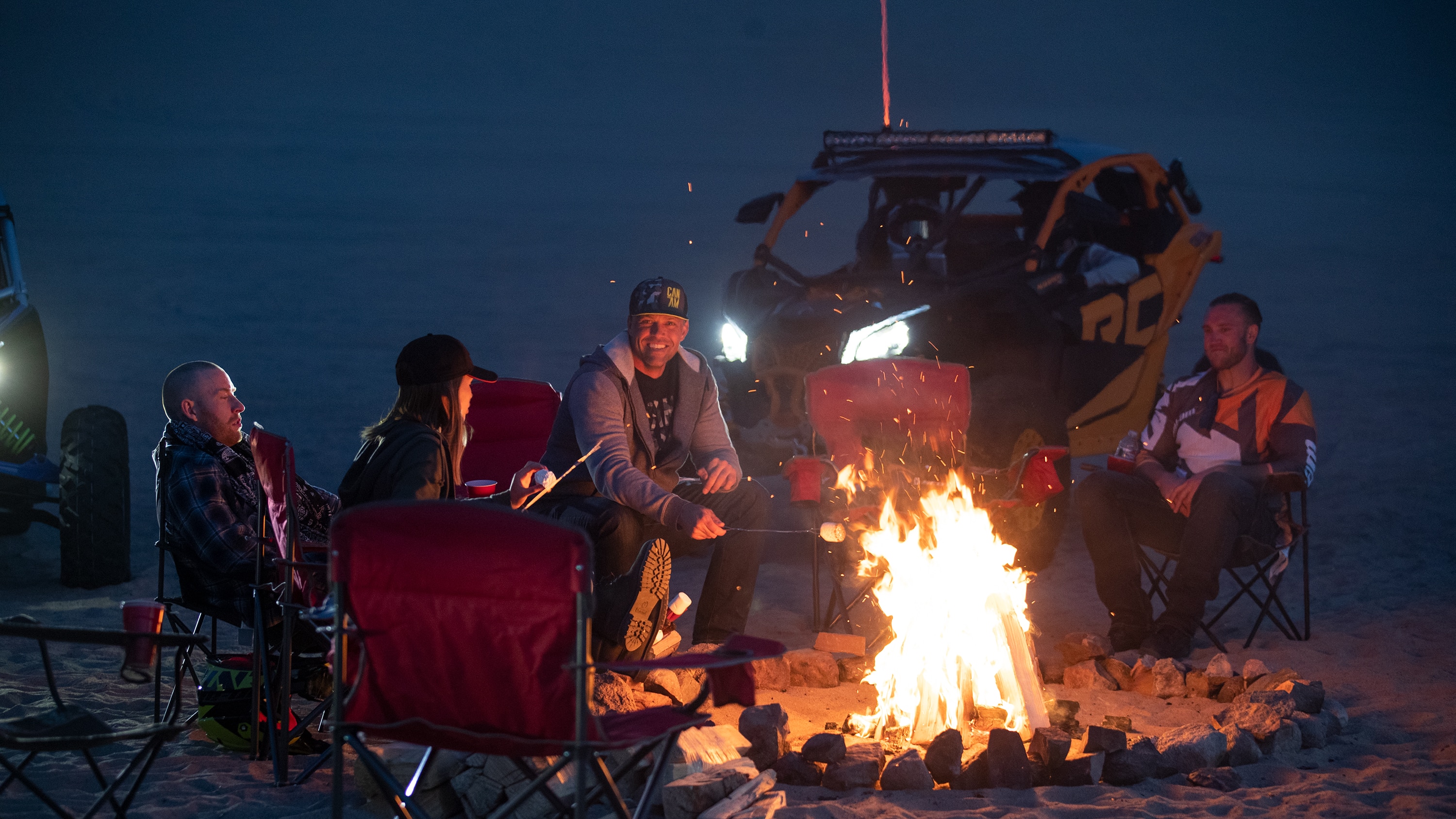 People around a campfire with a Can-Am Maverick Sport X rc in the back