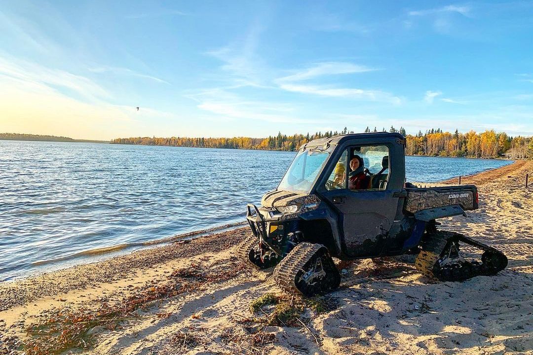 A Can-Am Defender Limited with track systems on sand near a lake