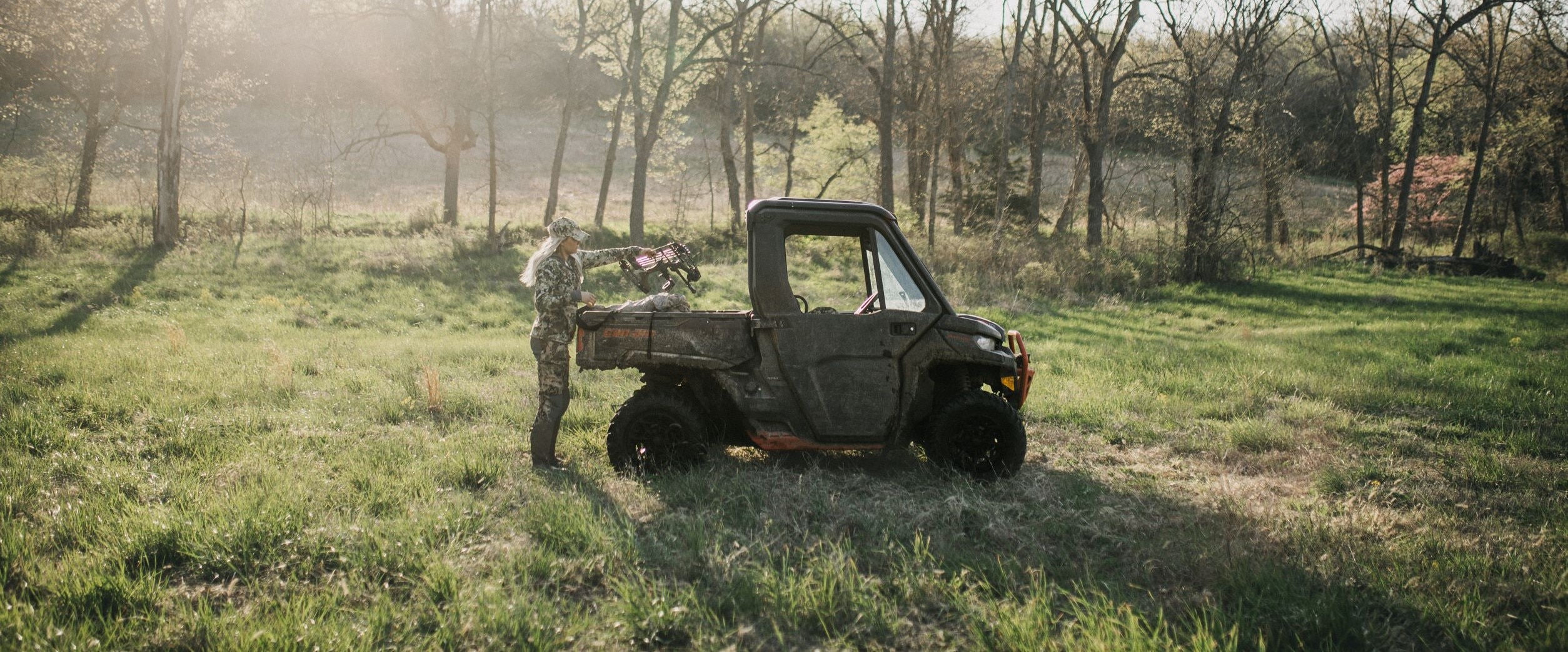 Alex Templeton dressed in camo, taking her cross-box out of the box of her Can-Am Defender in the early light of day. 