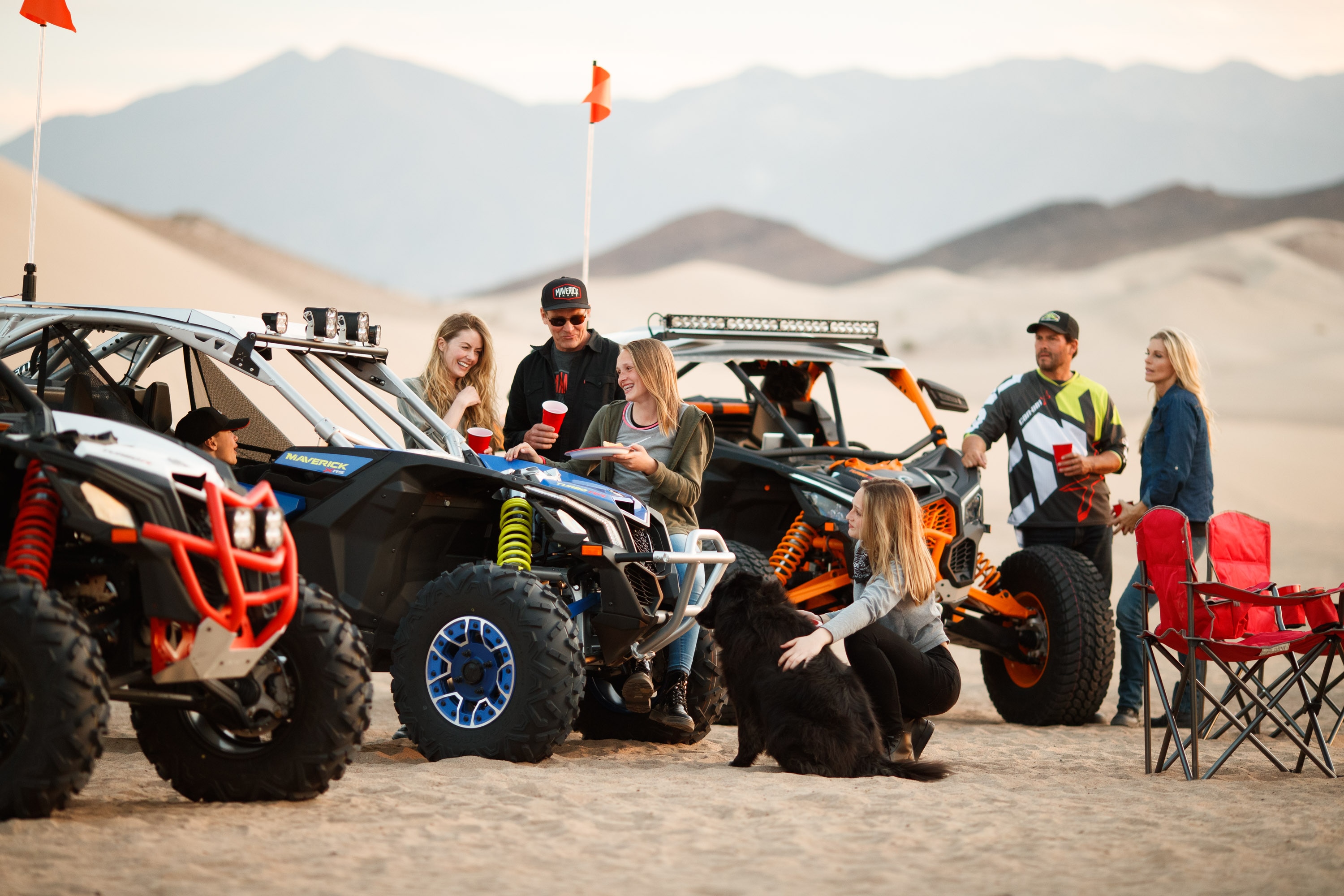 A bunch of people talking in the desert beside three 4-seater Can-Am Maverick X3 MAX side-by-side