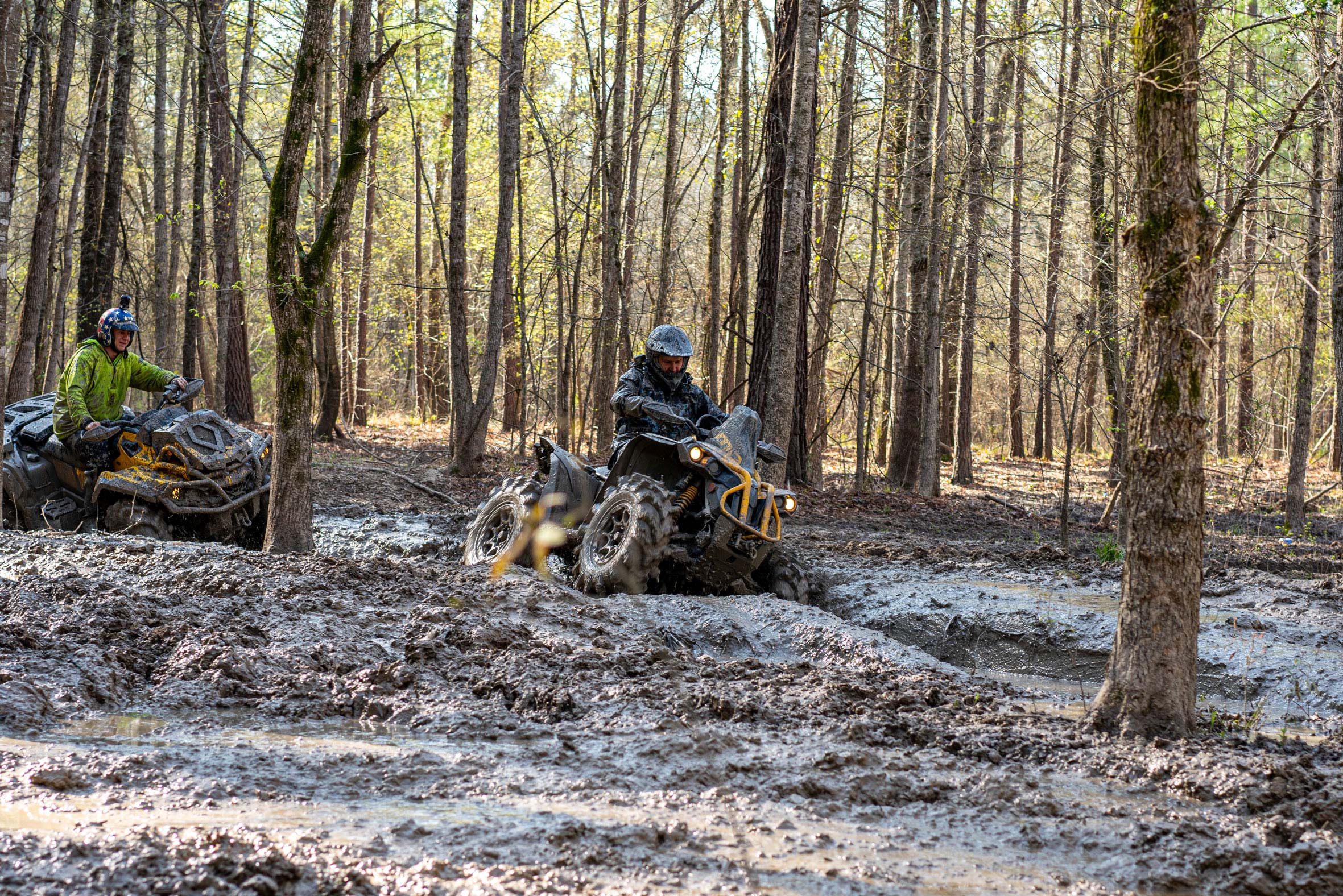 Two men riding new Can-Am X mr ATVs in the mud