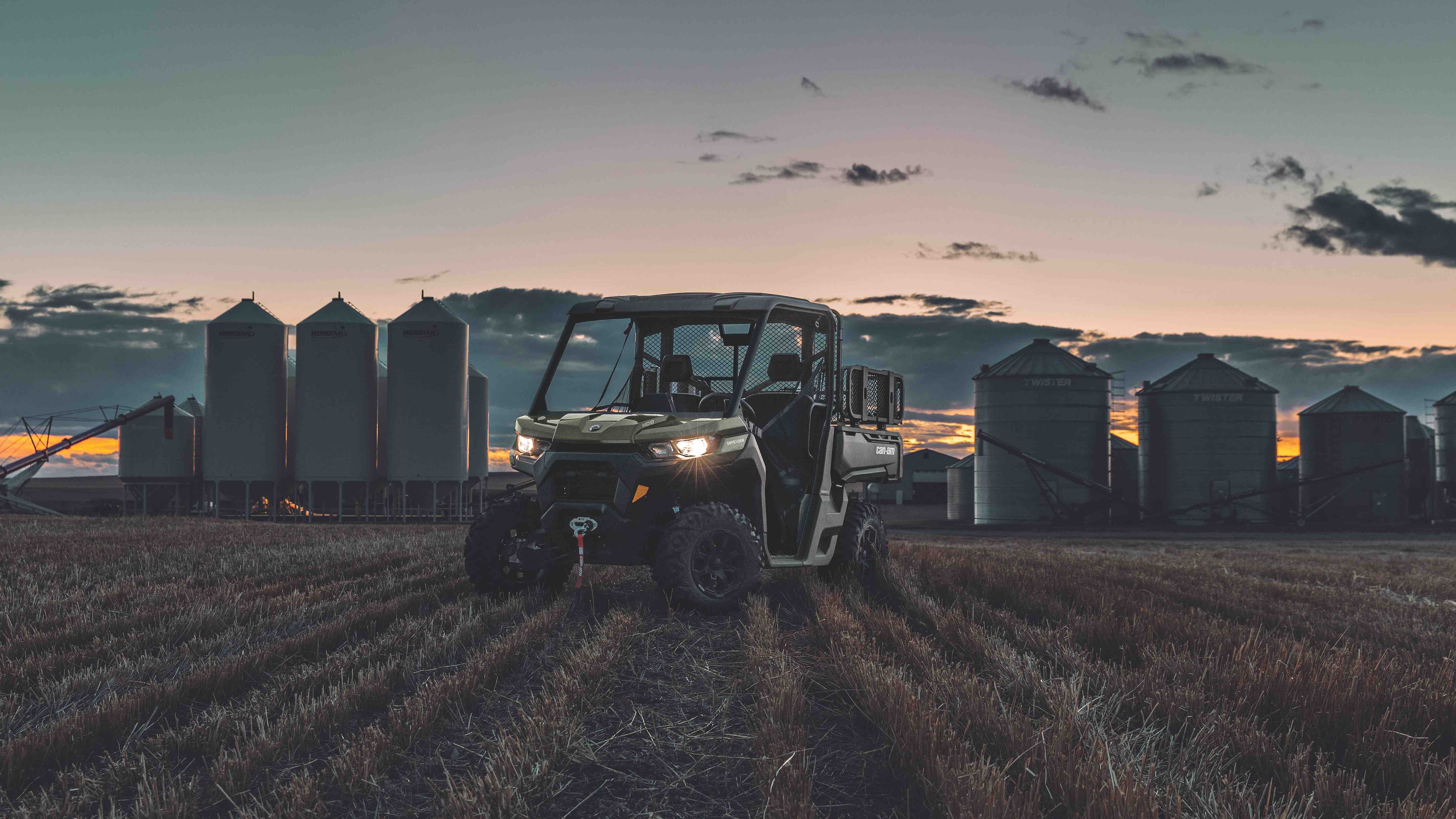 A Can-Am Defender DPS side-by-side on the land of a farm during sunset