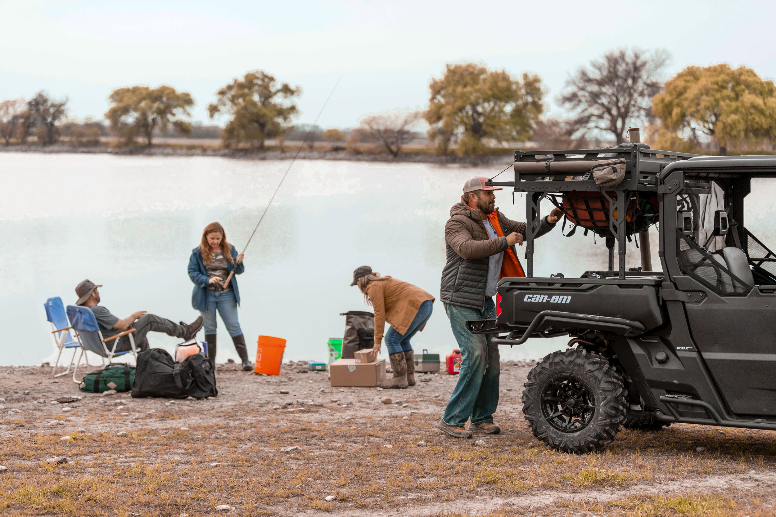 A man fishing with friends who picks up something from the back of his Can-Am Defender side-by-side