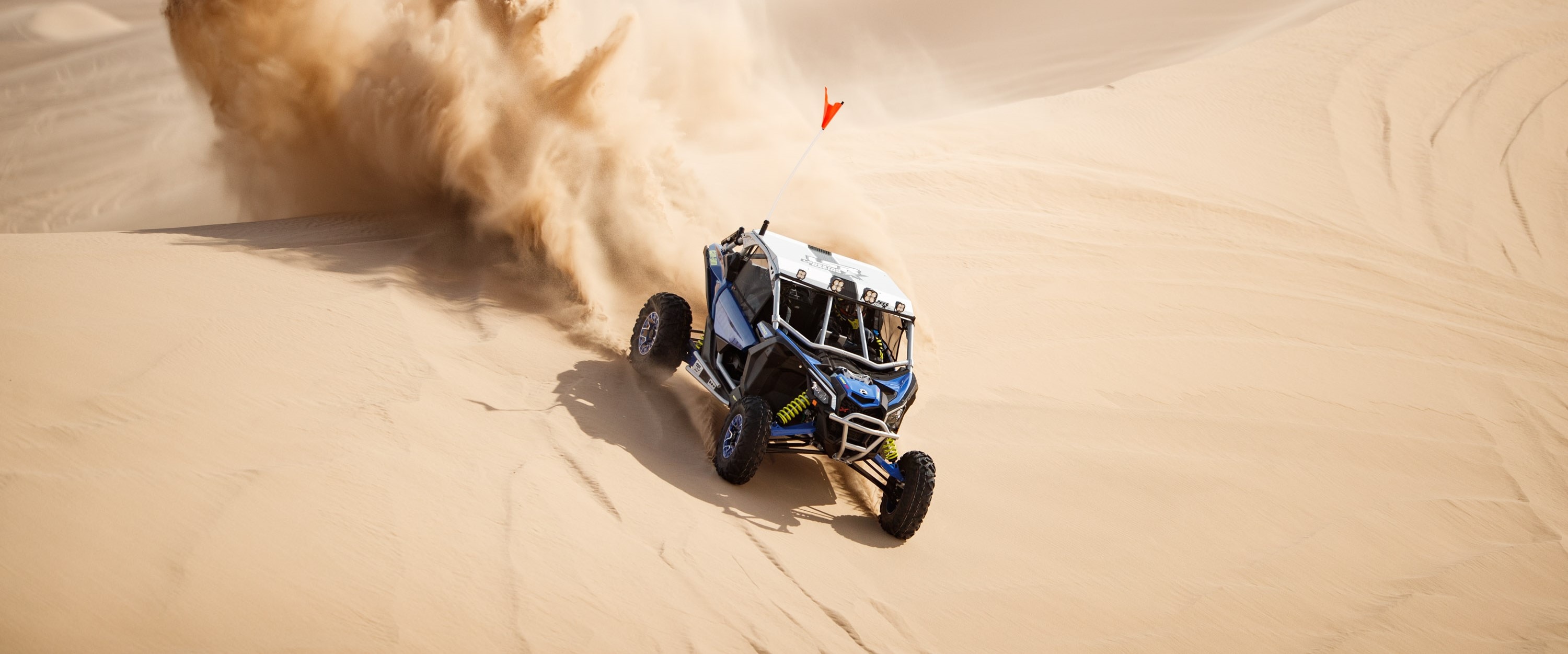 Maverick X3 RS TURBO RR racing through dunes, throwing up sand in its trail. 