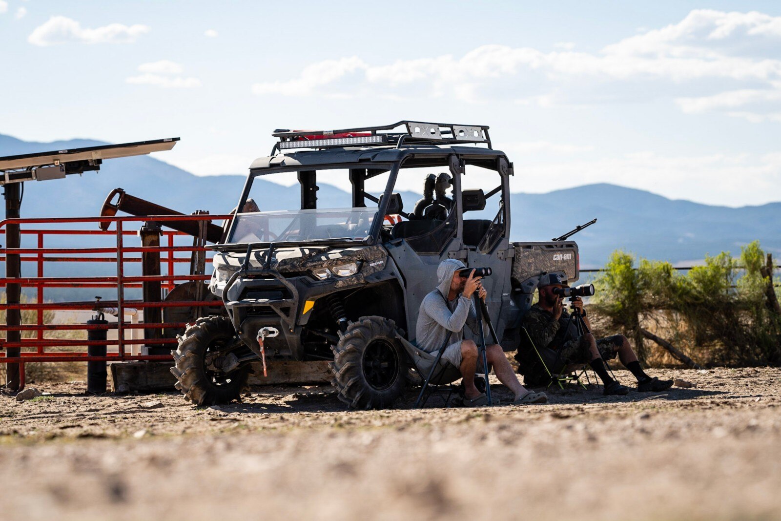Two riders sitting next to their Can-Am Defender Max XT, looking out at their fields through binoculars. 