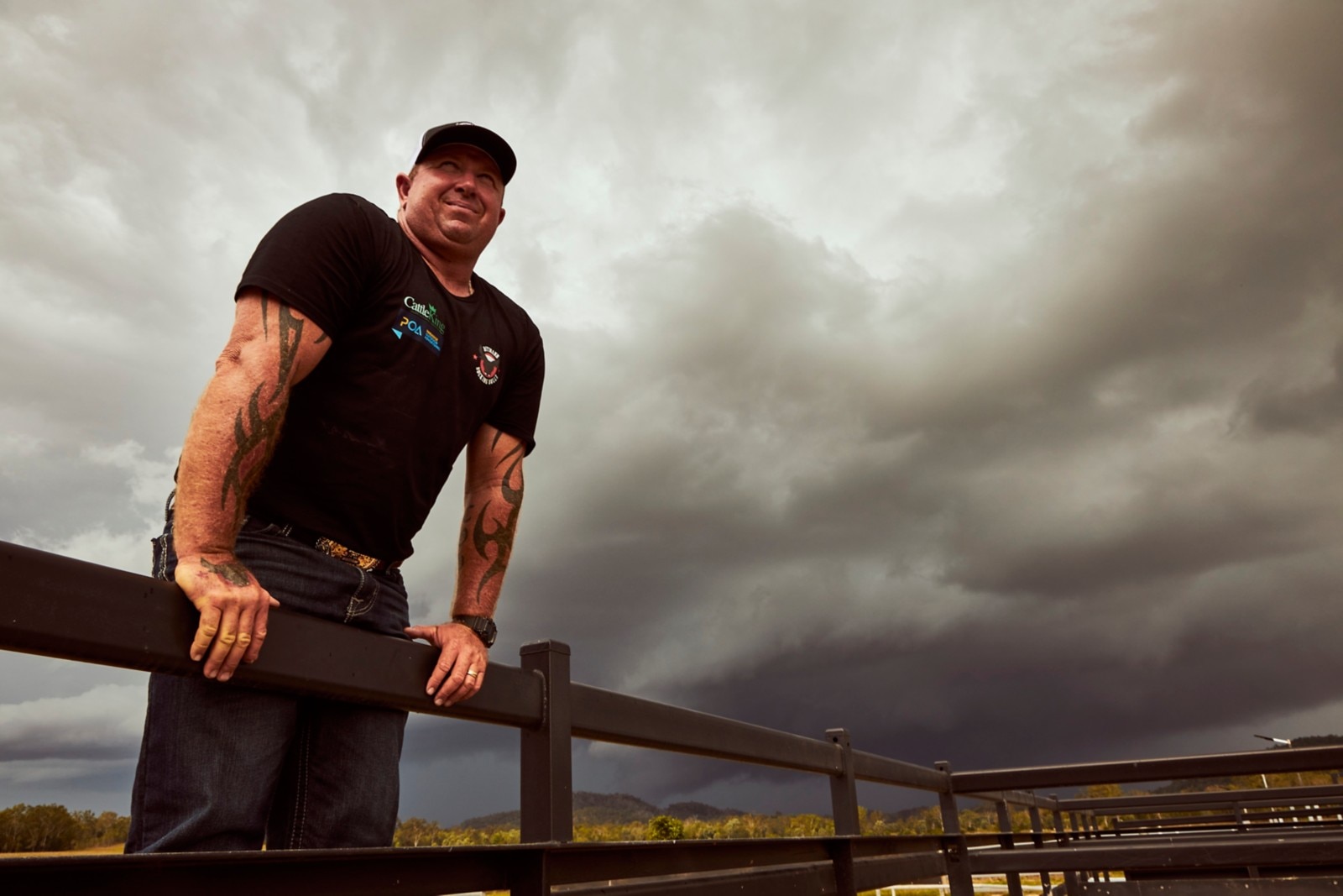 Jason Dittman standing on the bottom of his fence, looking up to dark clouds with sun shining through.