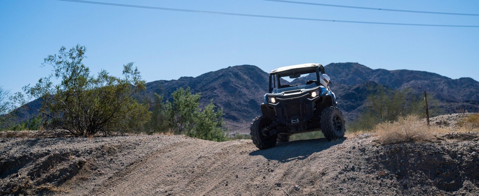 Front view of a Can-Am Defender driving between two rock walls in a desert setting