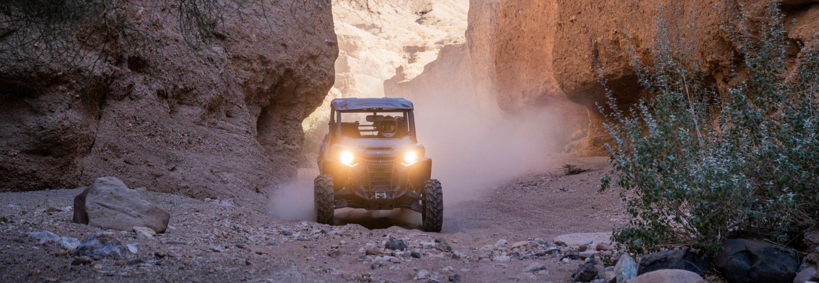 Front view of a Can-Am Commander driving between two rock walls in a desert setting