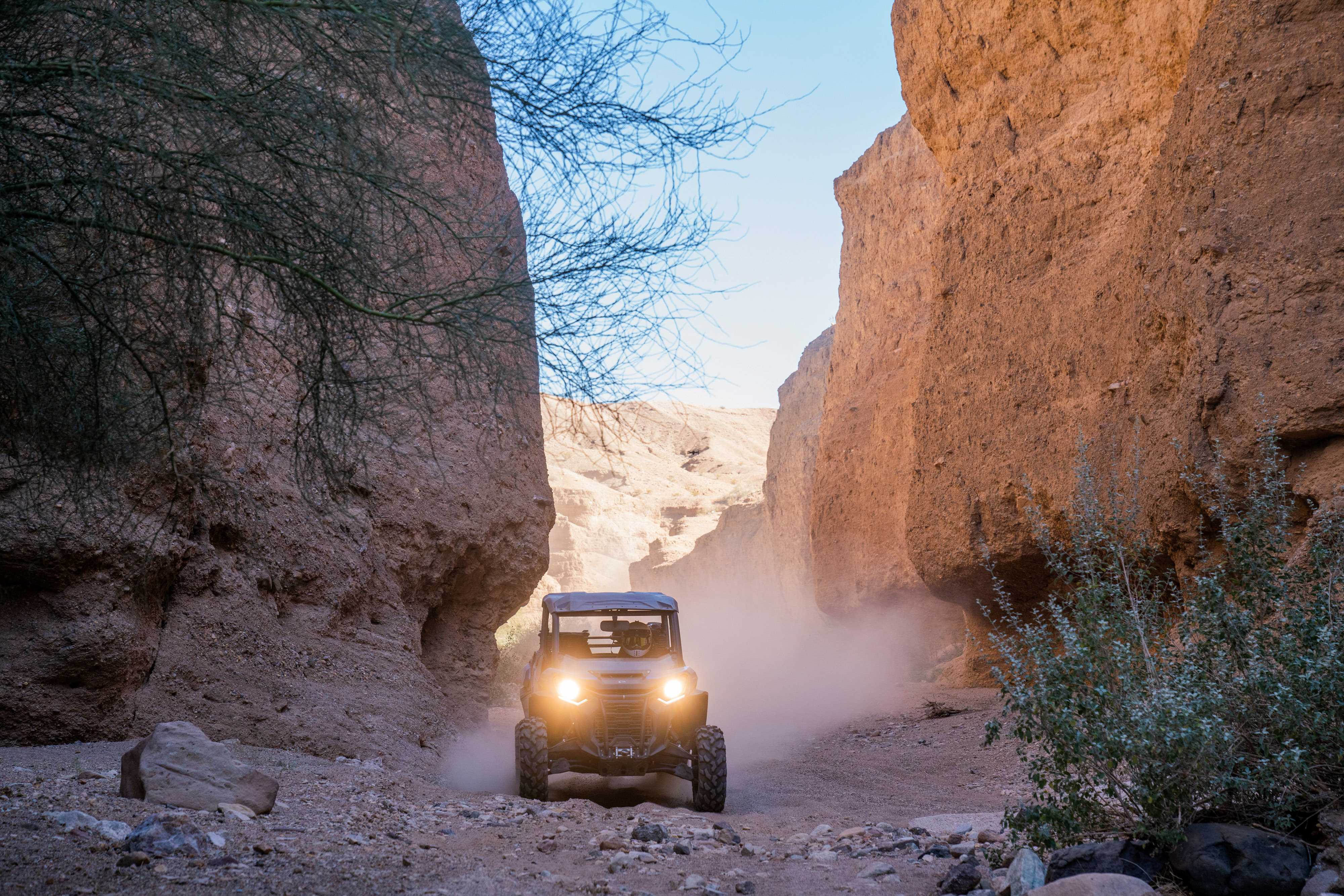 Front view of a Can-Am Defender driving between two rock walls in a desert setting. 