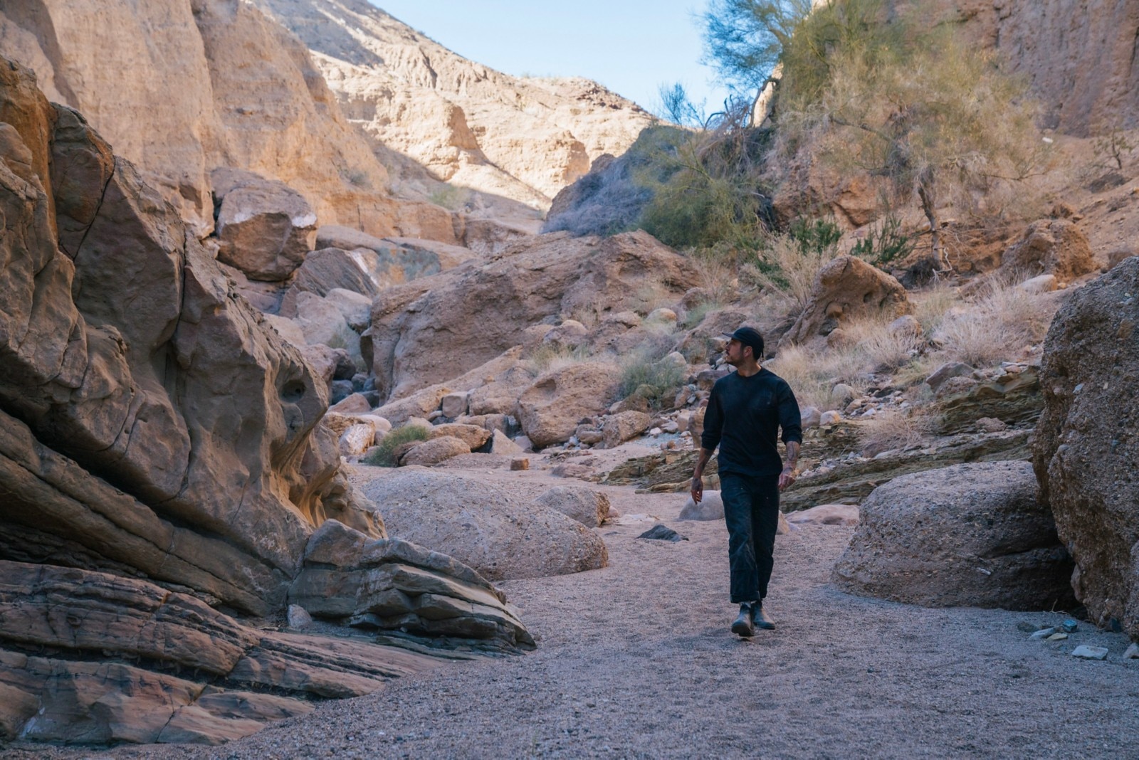 Carlos Naude caminando hacia la cámara, por un camino desierto, rodeado de rocas, mirando a su derecha.