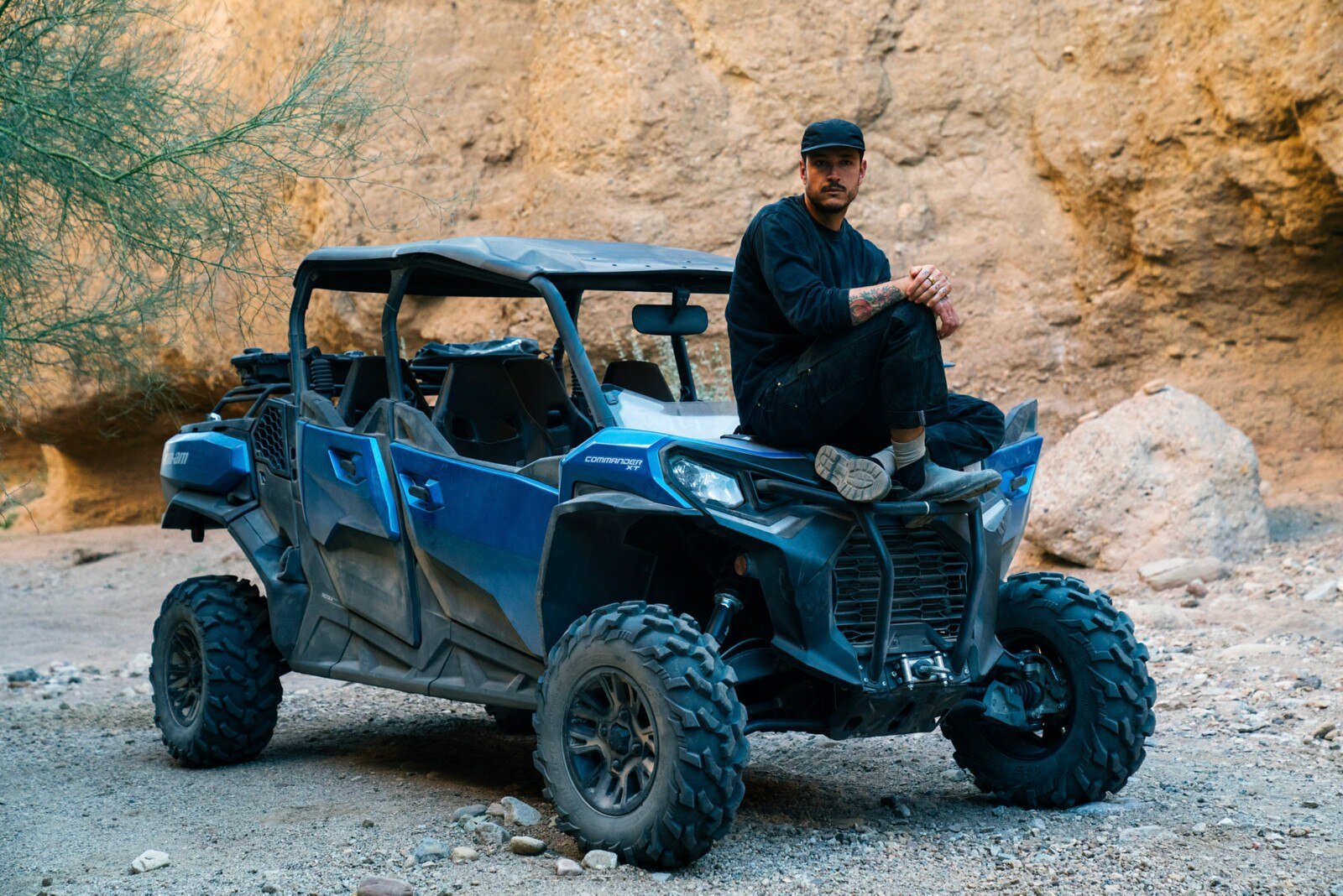 Carlos Naude sitting on the hood of his Oxford Blue Can-Am Commander MAX XT in front of a rock wall