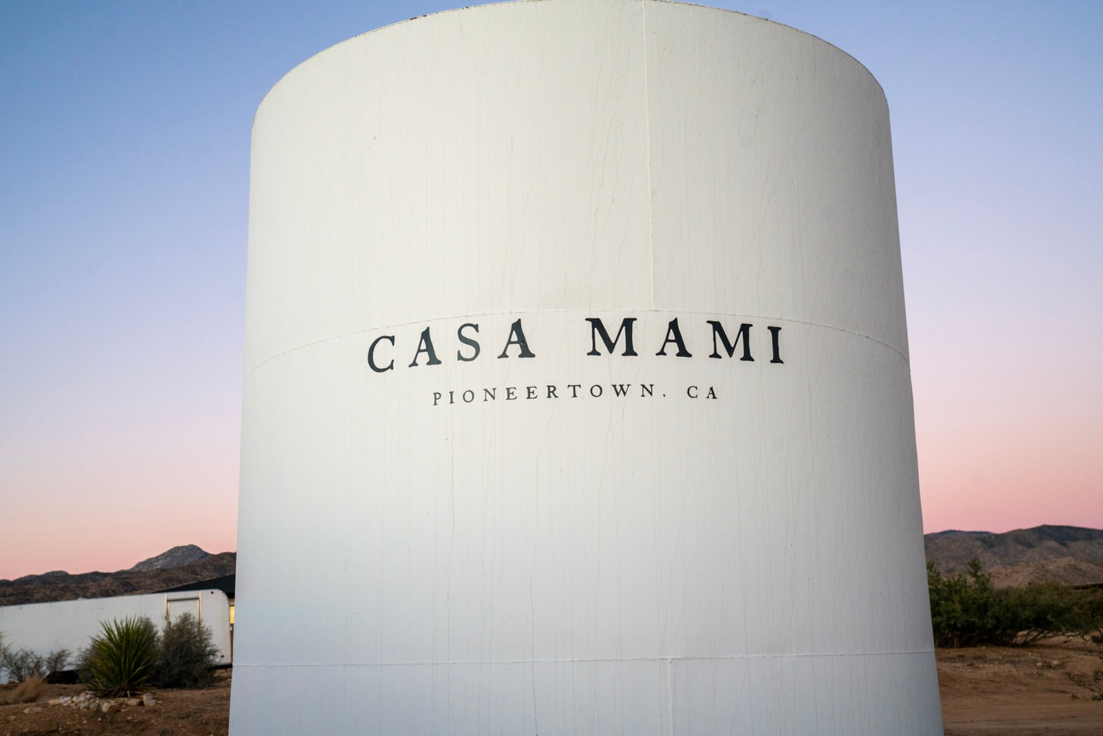 A tall white water reservoir with Carlos Naude's company name, Casa Mami, written on it
