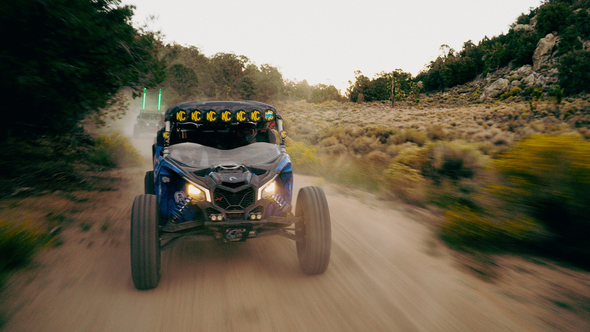 Riders speeding by inside their Can-Am Maverick X3 on a dirt of trail.