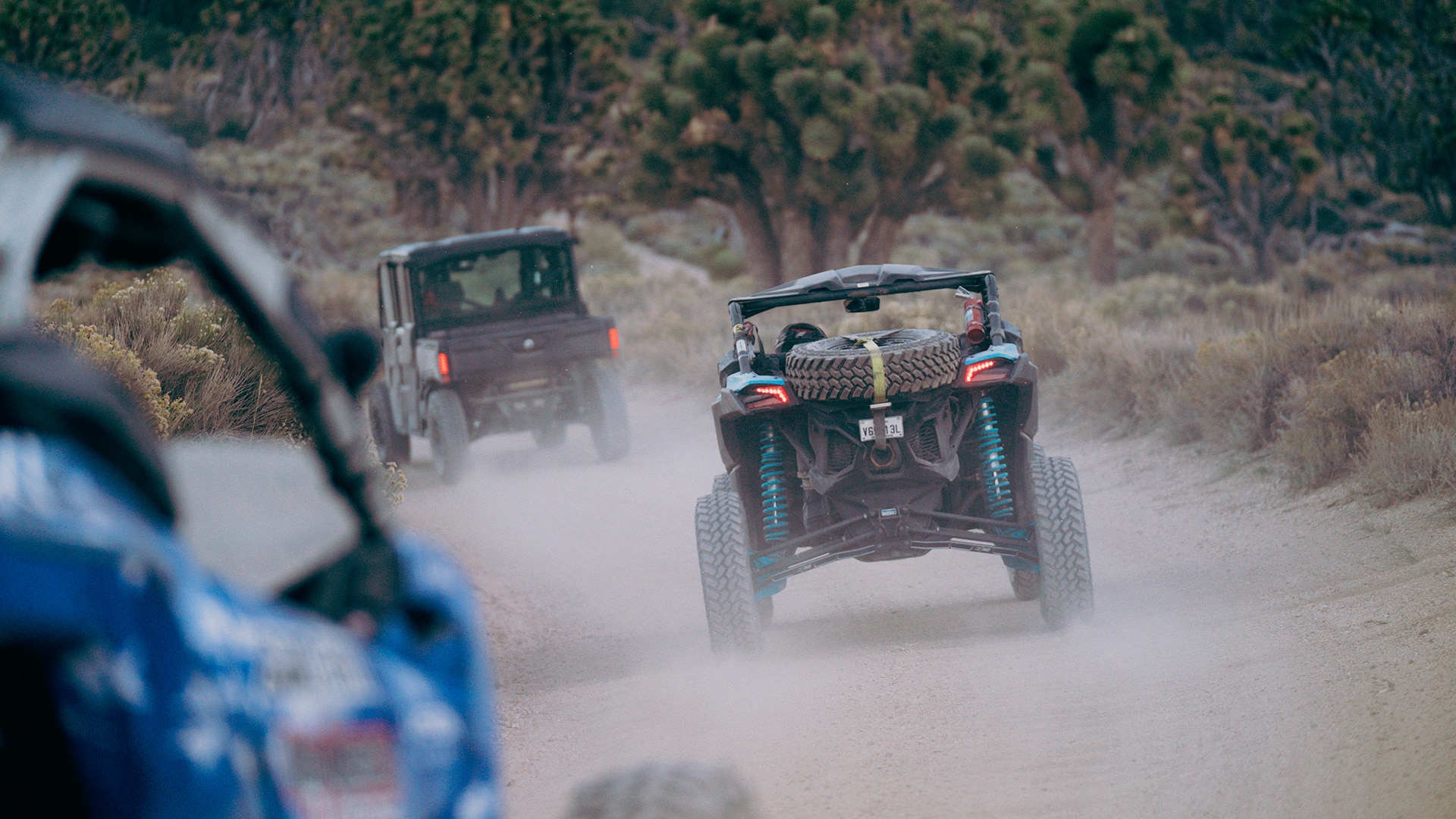 Riders driving Can-Am side-by-sides on a trail of dirt and kicking up clouds of dust.