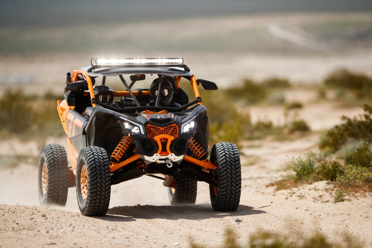 A Can-Am Maverick X3, equipped with a light bar, winch and other Can-Am accessories, driving in a desert setting