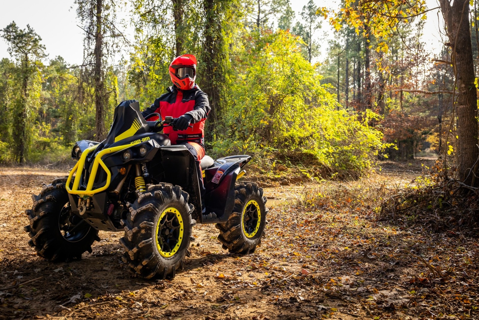 Rider assis sur leur Can-Am Renegade X MR jaune vêtu d'un équipement de boue Finntrail et d'un casque Pyra, devant un fond boisé.