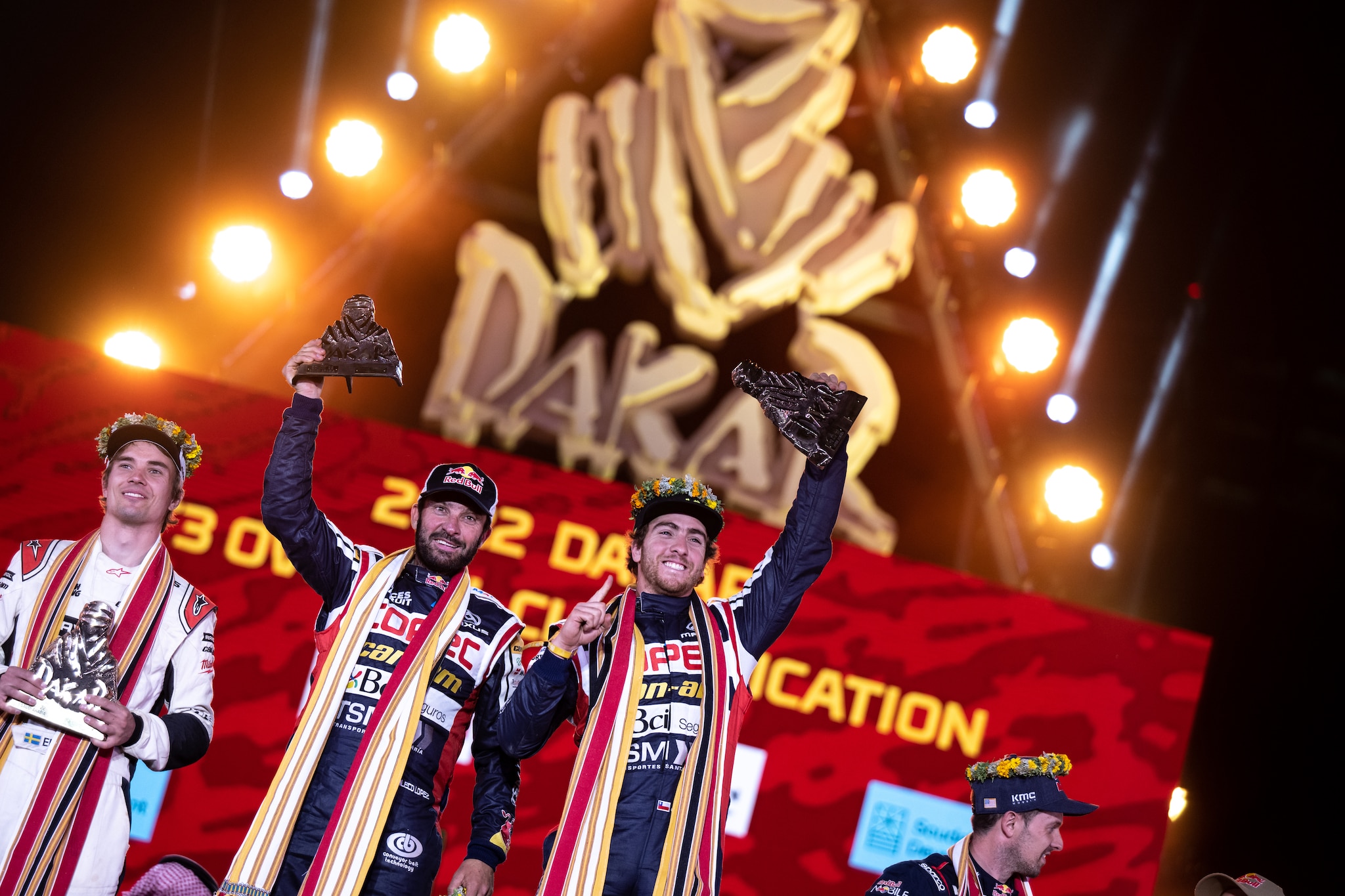 Can-Am riders celebrating another win on the podium with the Dakar sign in the backdrop. 