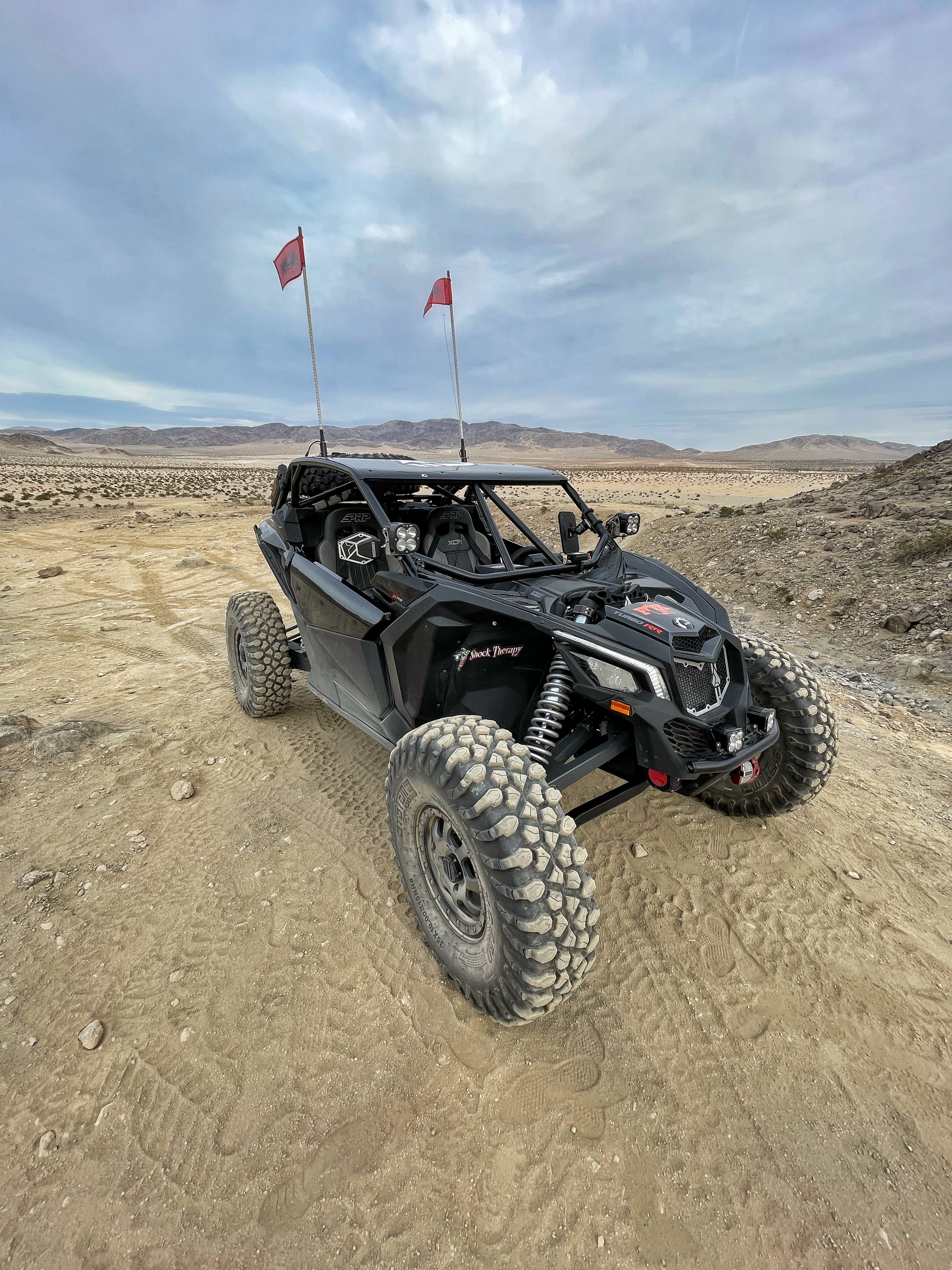 Custom-built black Can-Am side-by-side idling in the dirt with two red pennants.